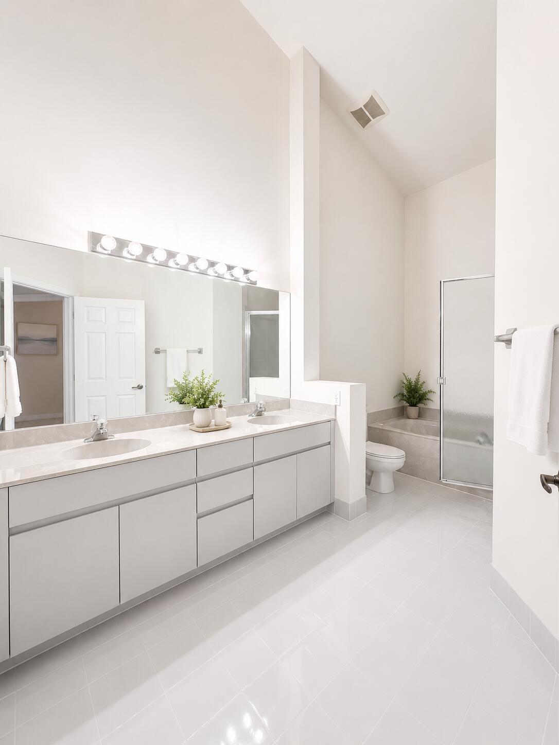 Double vanity featuring light-gray toned cabinetry, dual drop-in sinks, a large wall-spanning mirror, and high vaulted ceilings with a glass-enclosed shower and tub combination
