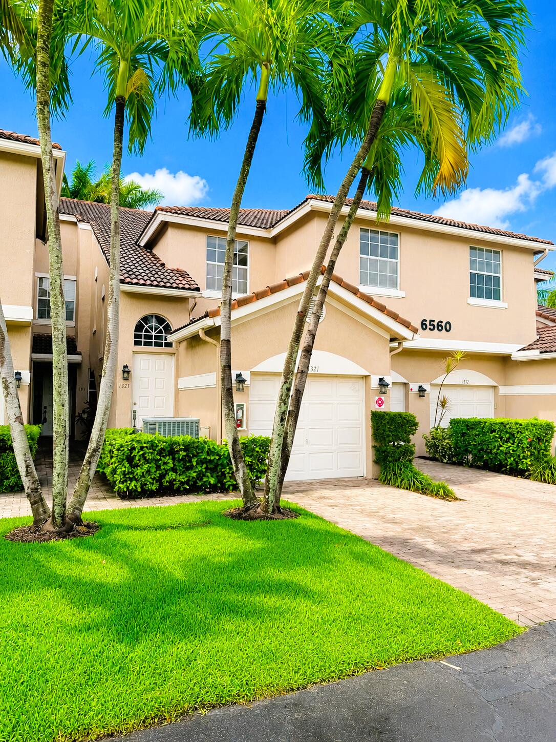 Two-story exterior featuring a stucco faade, a tiled roof, a paved driveway, and established palm tree landscaping