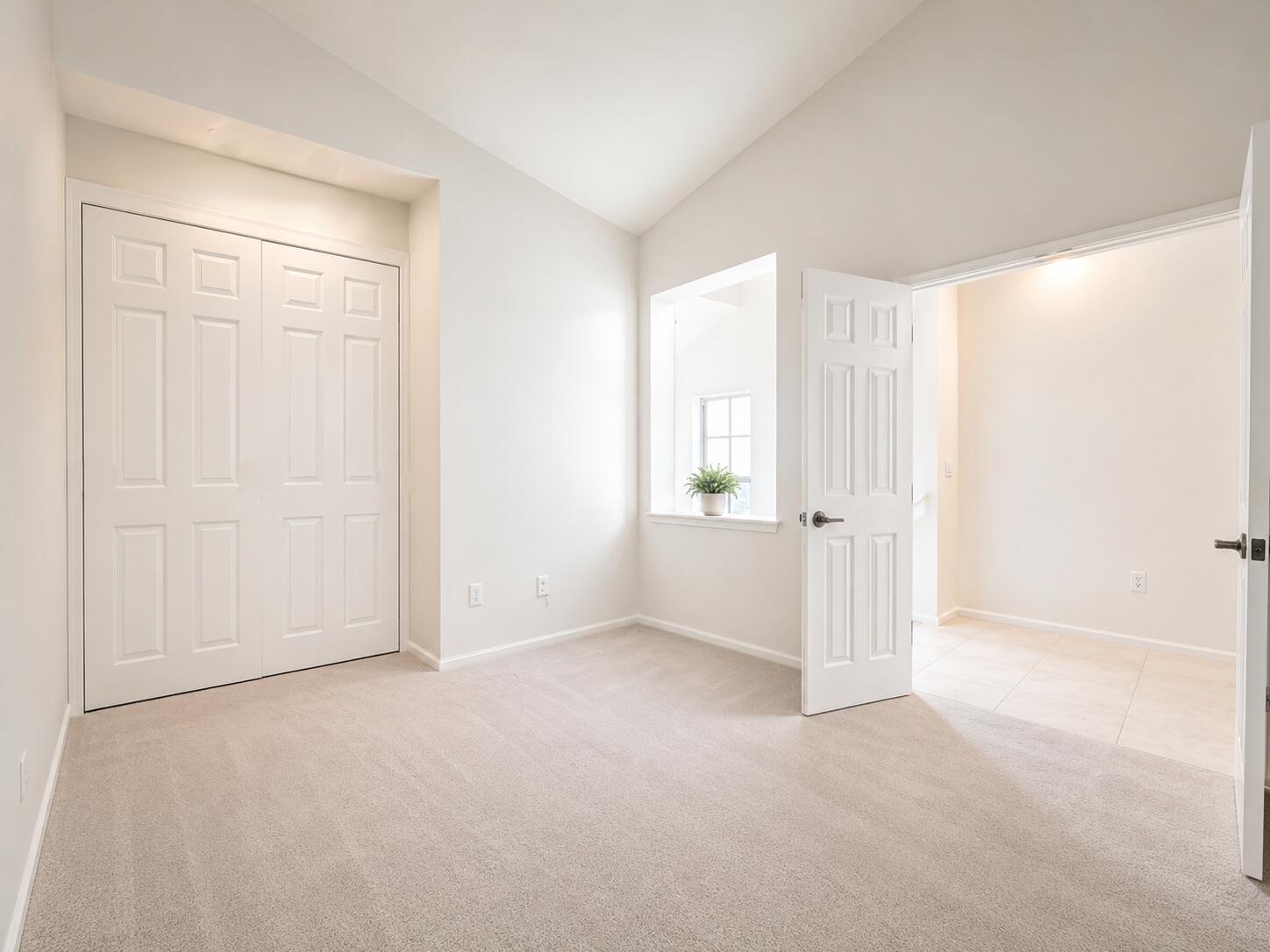 Vaulted ceiling, neutral wall-to-wall carpeting, recessed window sill, and multi-panel interior doors