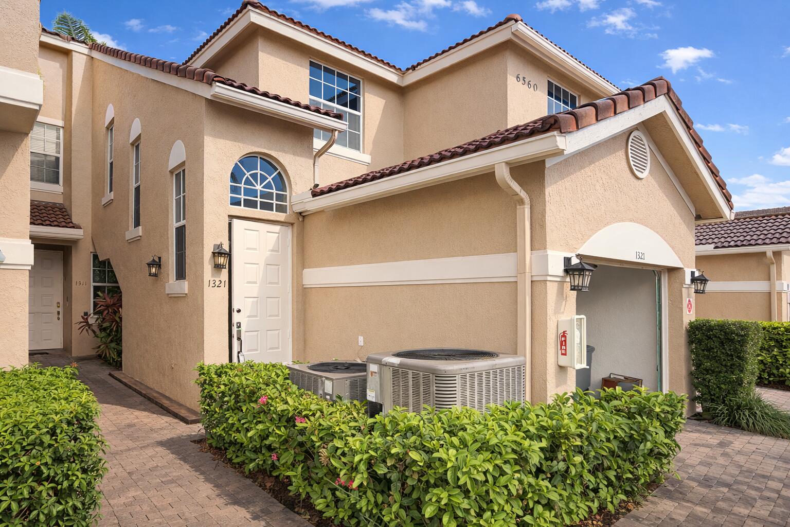 Stucco exterior featuring arched accent windows, tile roofing, an integrated garage, and paver walkway