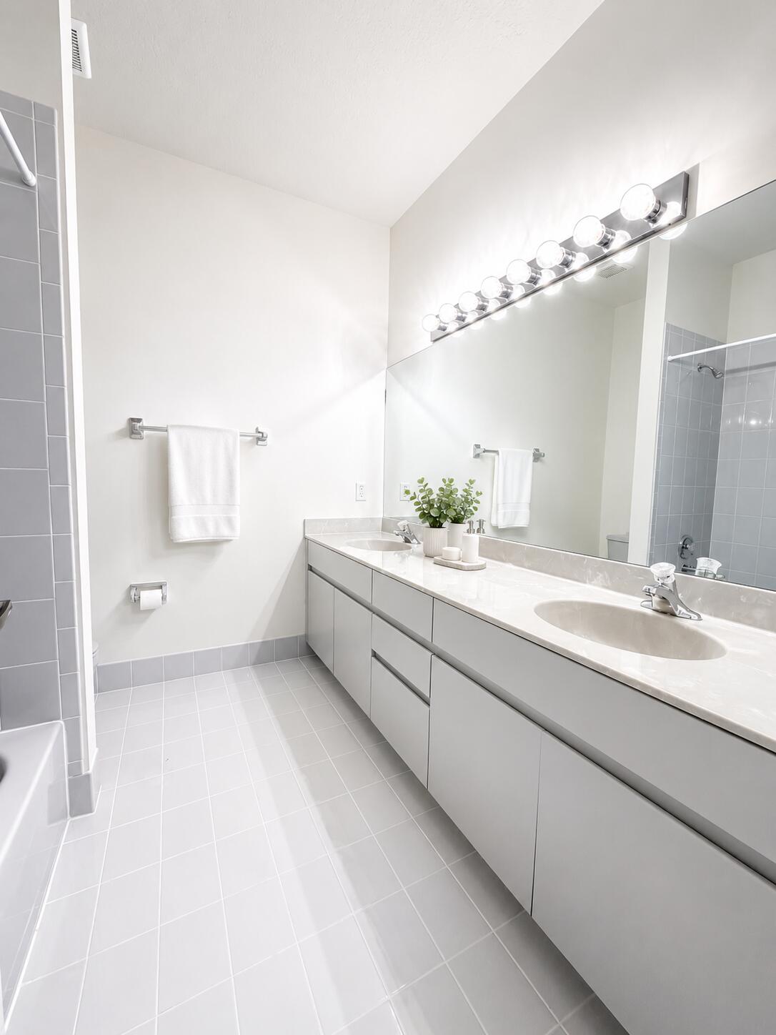 Double vanity featuring slab-front cabinetry, stone-finish countertops, undermount sinks, and a large-format vanity mirror with integrated multi-bulb lighting