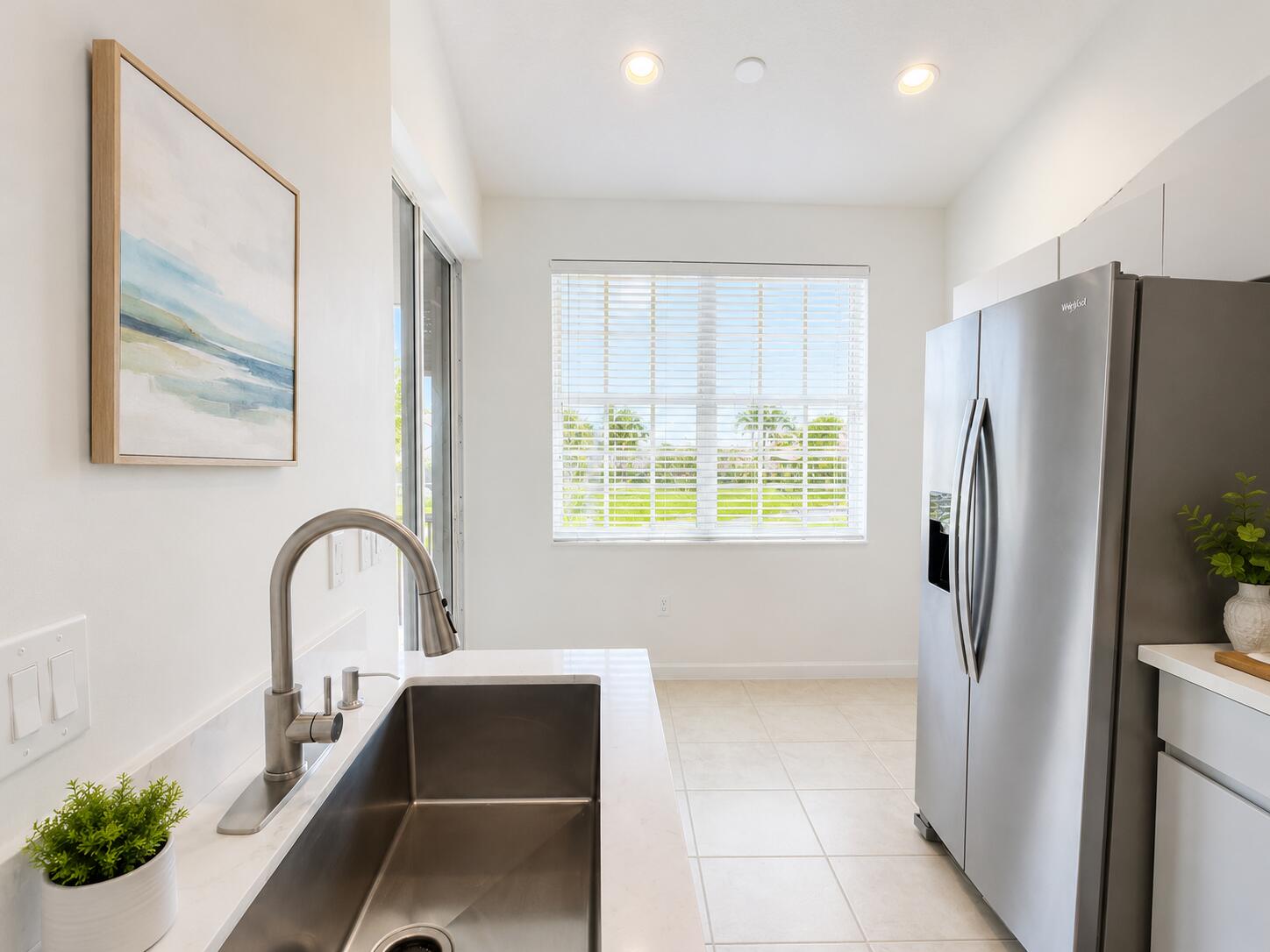 Stainless steel refrigerator, undermount rectangular kitchen sink with a high-arc pull-down faucet, quartz countertops, tile flooring, and recessed ceiling lighting