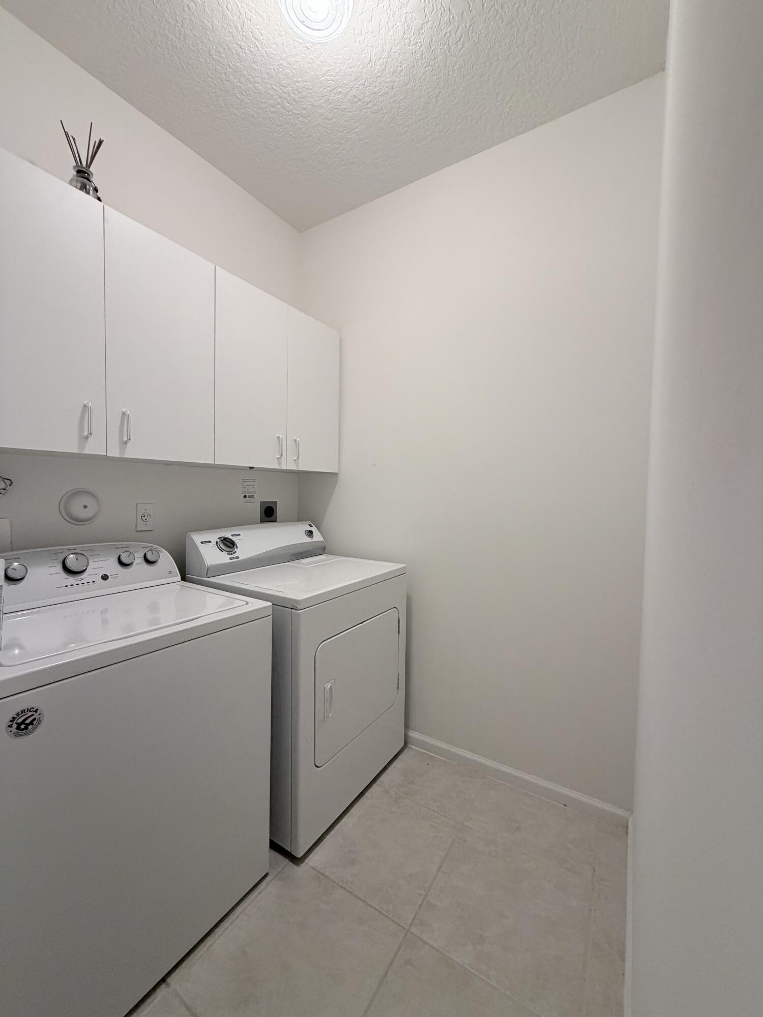 Utility space featuring white shaker-style wall-mounted cabinetry, tile flooring, and overhead lighting
