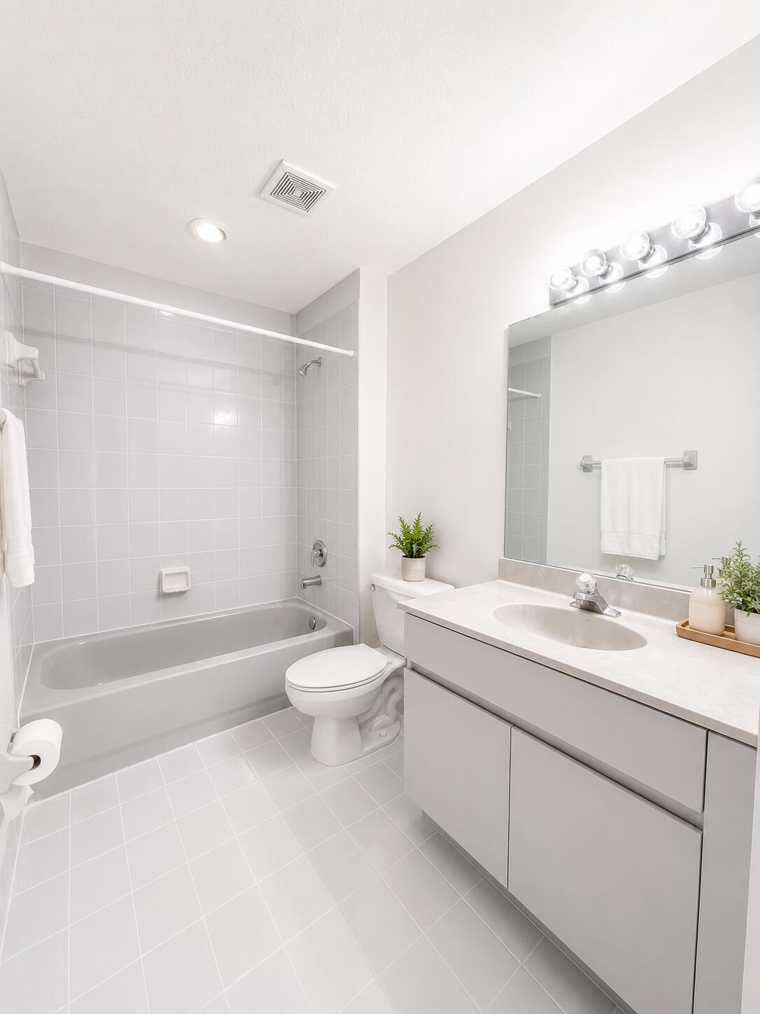 Bathroom featuring a vanity with a light-toned countertop, integrated basin, wall-to-wall mirror, tiled bathtub surround, and light-toned tile flooring