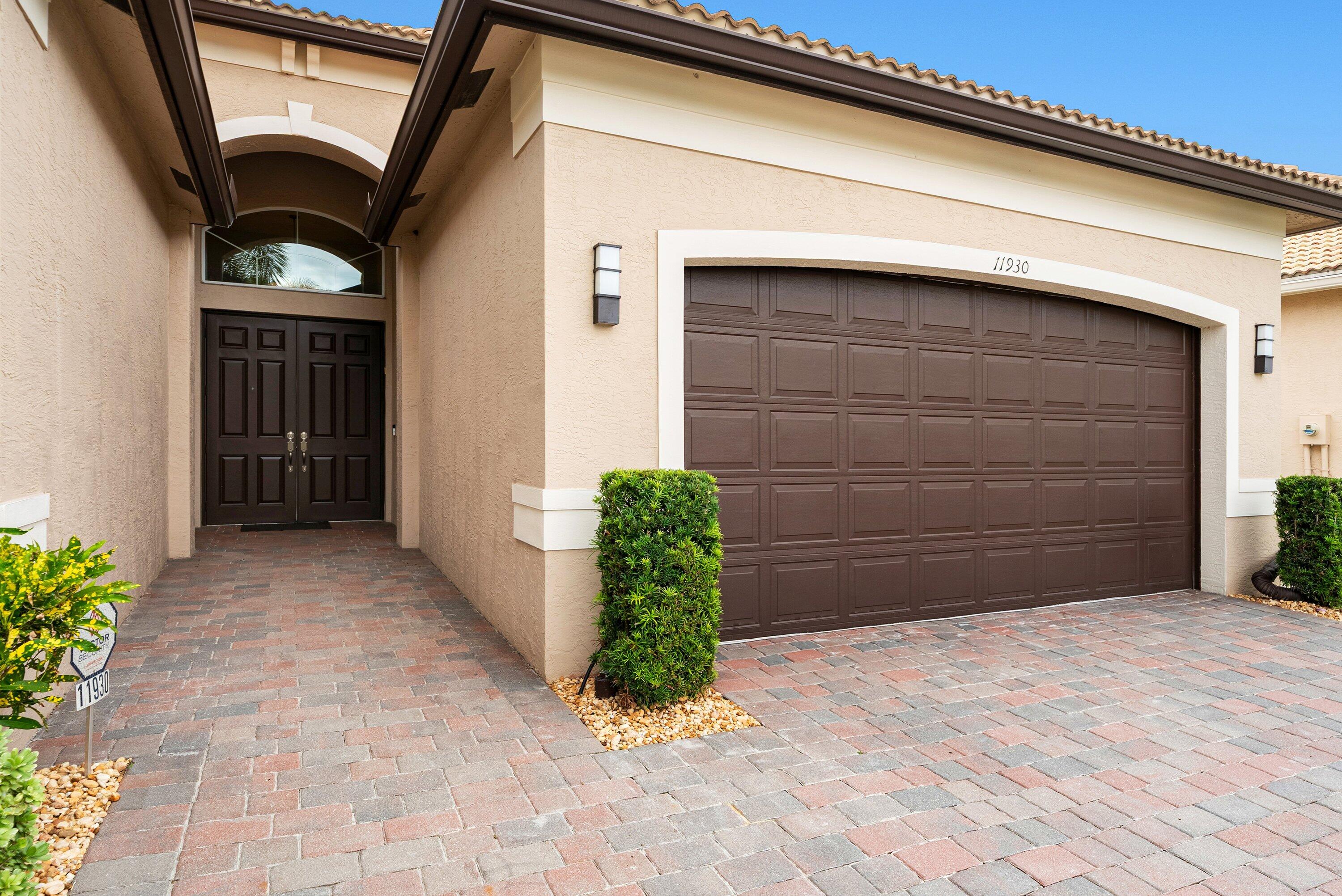Stucco exterior featuring an arched entryway, double-panel front doors with a fanlight window, a multi-car garage with a raised-panel door, and a decorative paver driveway Stucco exterior featuring an arched entryway, double-panel front doors with a fanlight window, a multi-car garage with a raised-panel door, and a decorative paver driveway
