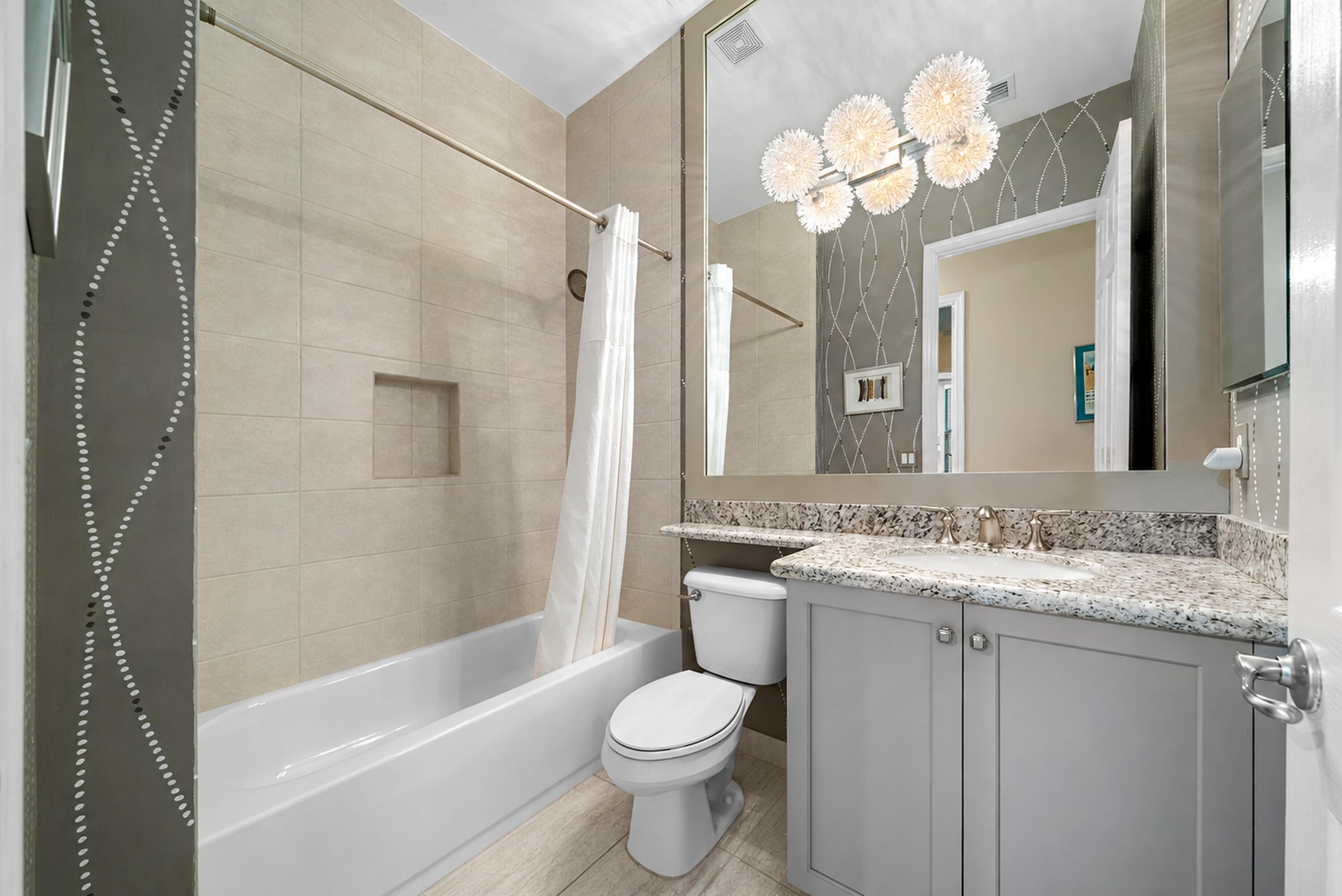 Bathroom featuring a vanity with stone countertop, integrated sink, large wall-mounted mirror, multi-light fixture, and tub with tiled surround and inset wall niche