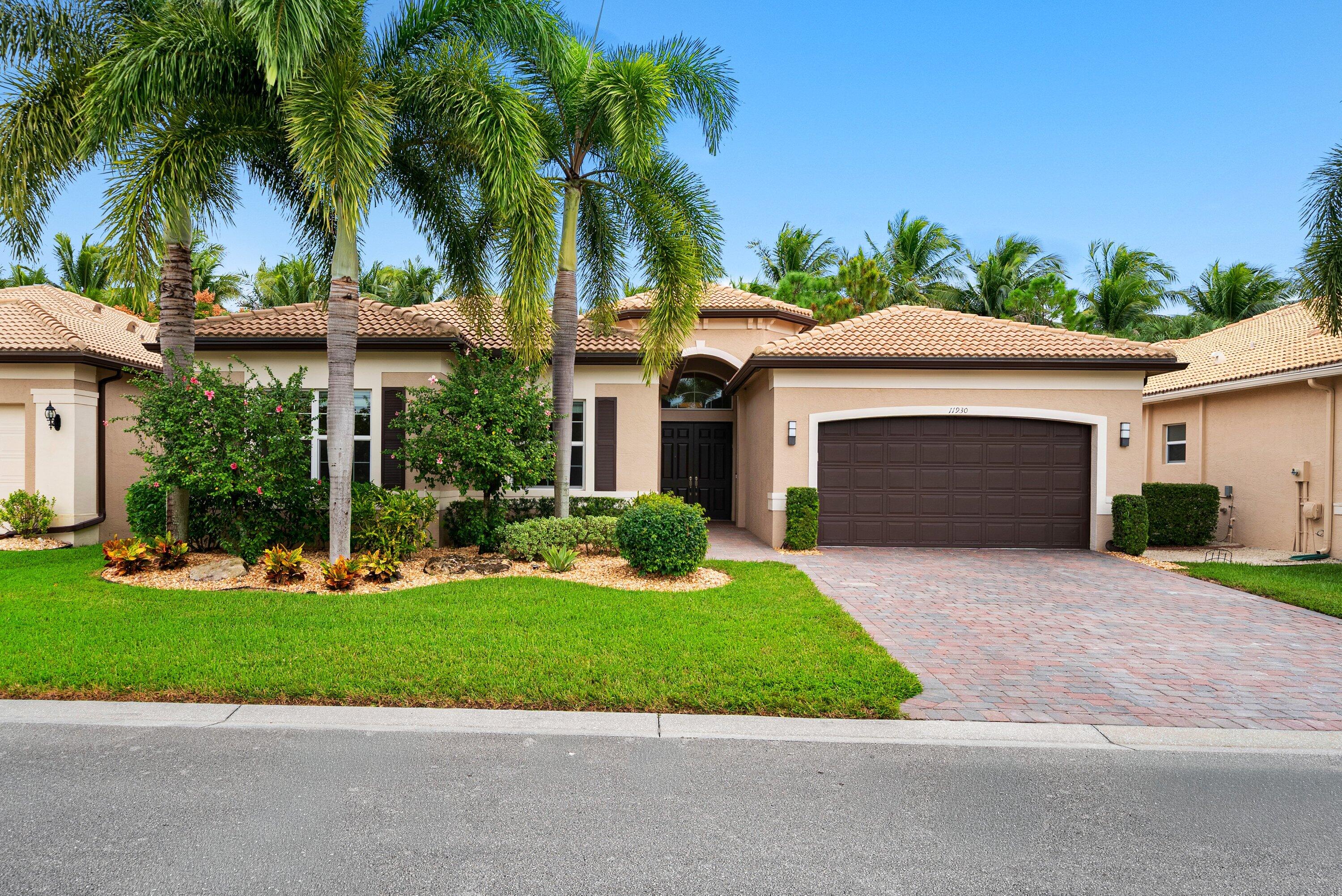 Stucco exterior featuring a multi-hipped tile roof, paver driveway, attached two-car garage, and mature palm trees Stucco exterior featuring a multi-hipped tile roof, paver driveway, attached two-car garage, and mature palm trees