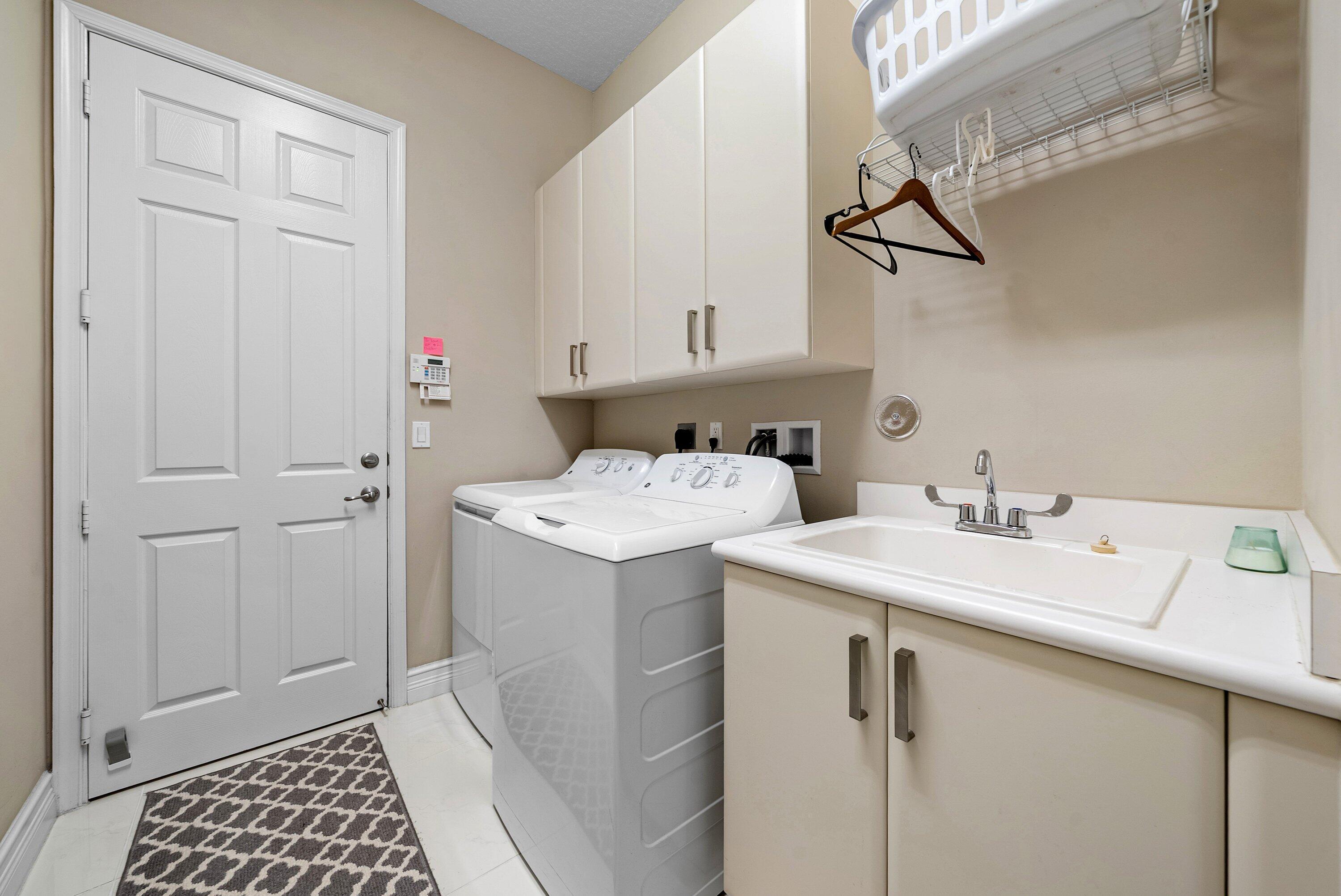 Utility room featuring upper cabinetry, a base cabinet with an integrated basin, a faucet, and white tile flooring