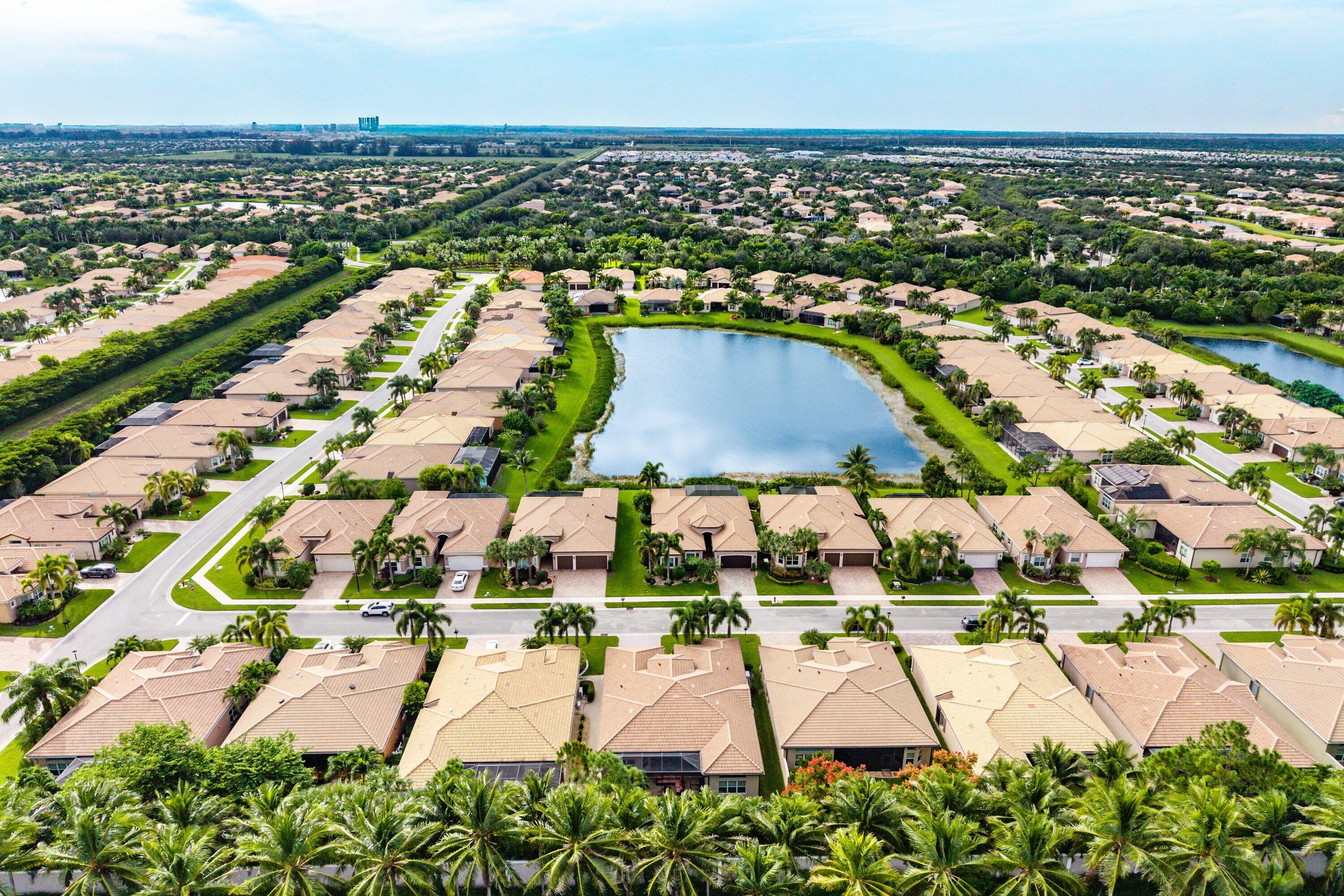 Aerial perspective of a residential community centered around a large lake, featuring multiple tile-roof homes, paved street infrastructure, and established landscaping