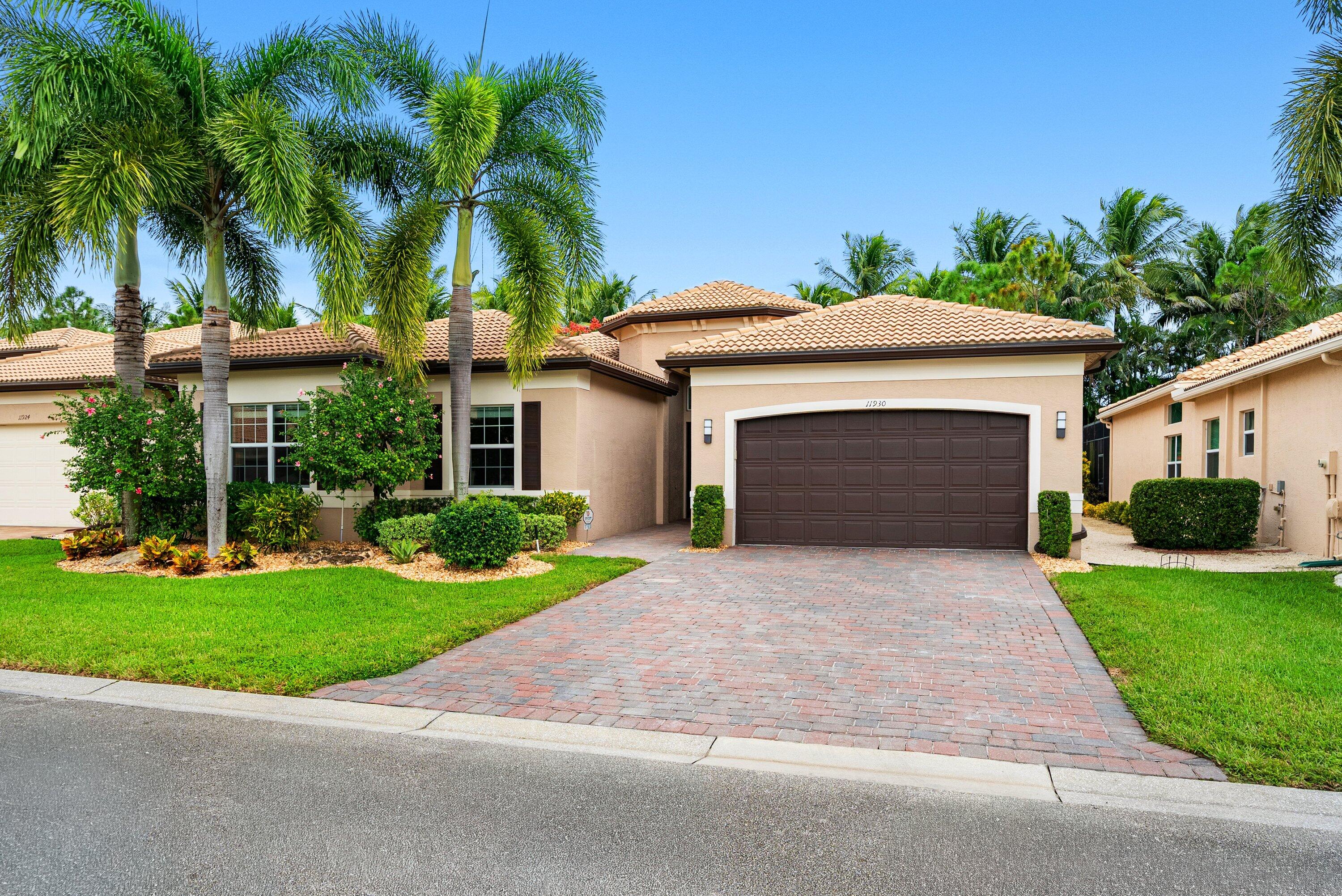 Stucco exterior residence featuring a multi-hipped tile roof, paver driveway, arched garage entry, and mature palm landscaping Stucco exterior residence featuring a multi-hipped tile roof, paver driveway, arched garage entry, and mature palm landscaping