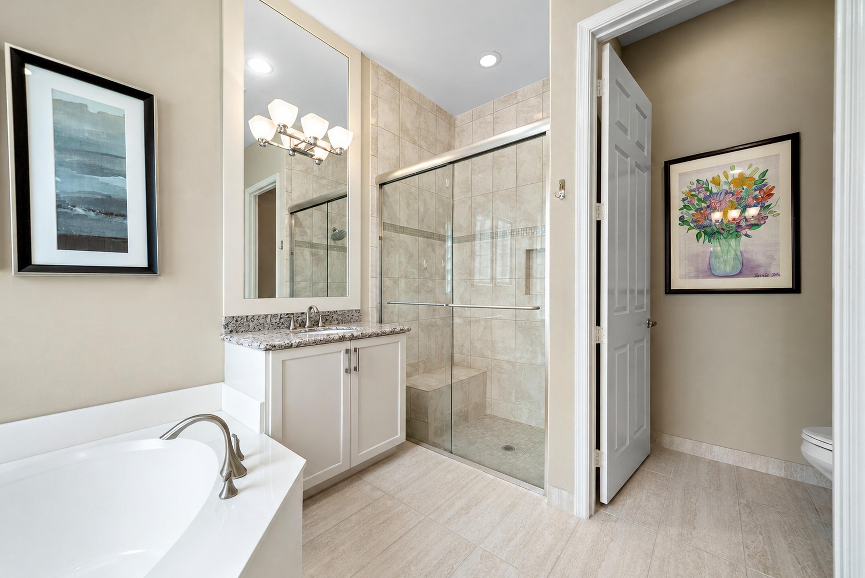 Bathroom featuring a walk-in shower with a glass enclosure and built-in bench, a soaking tub, a vanity with stone-finish countertop, and tiled flooring