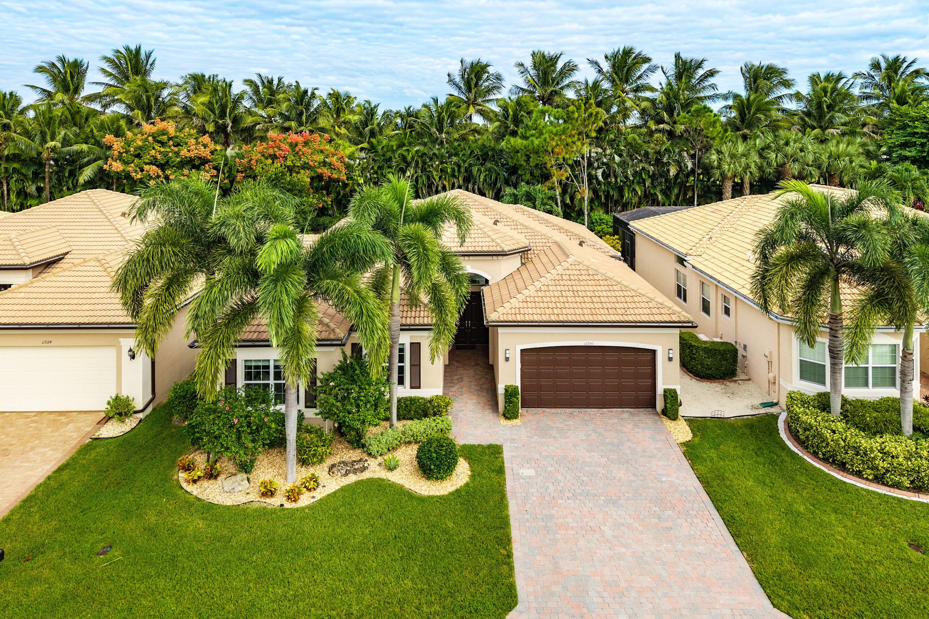 Stucco exterior featuring a multi-hipped tile roof, paver driveway, attached two-car garage, and mature palm tree landscaping