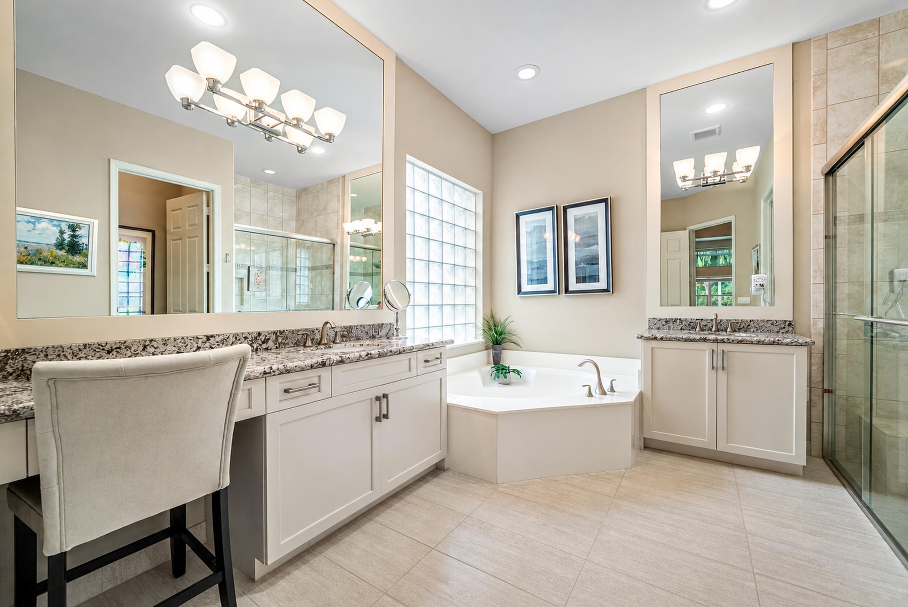 Bathroom featuring dual white cabinetry with stone countertops, a corner soaking tub, glass block window, and glass-enclosed shower