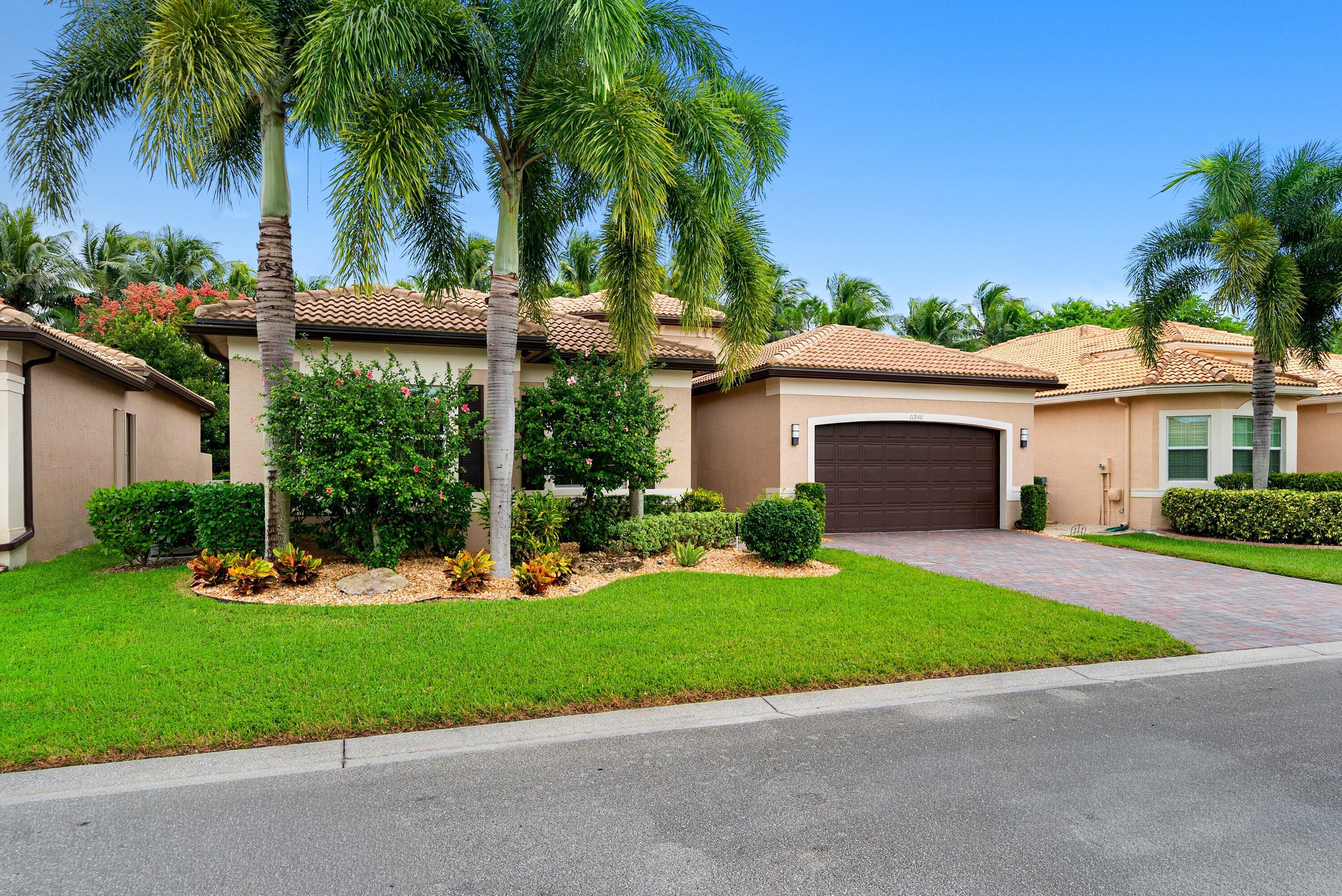 Stucco exterior residence featuring a tile roof, paved driveway, two-car garage, and established landscaping with mature palm trees Stucco exterior residence featuring a tile roof, paved driveway, two-car garage, and established landscaping with mature palm trees