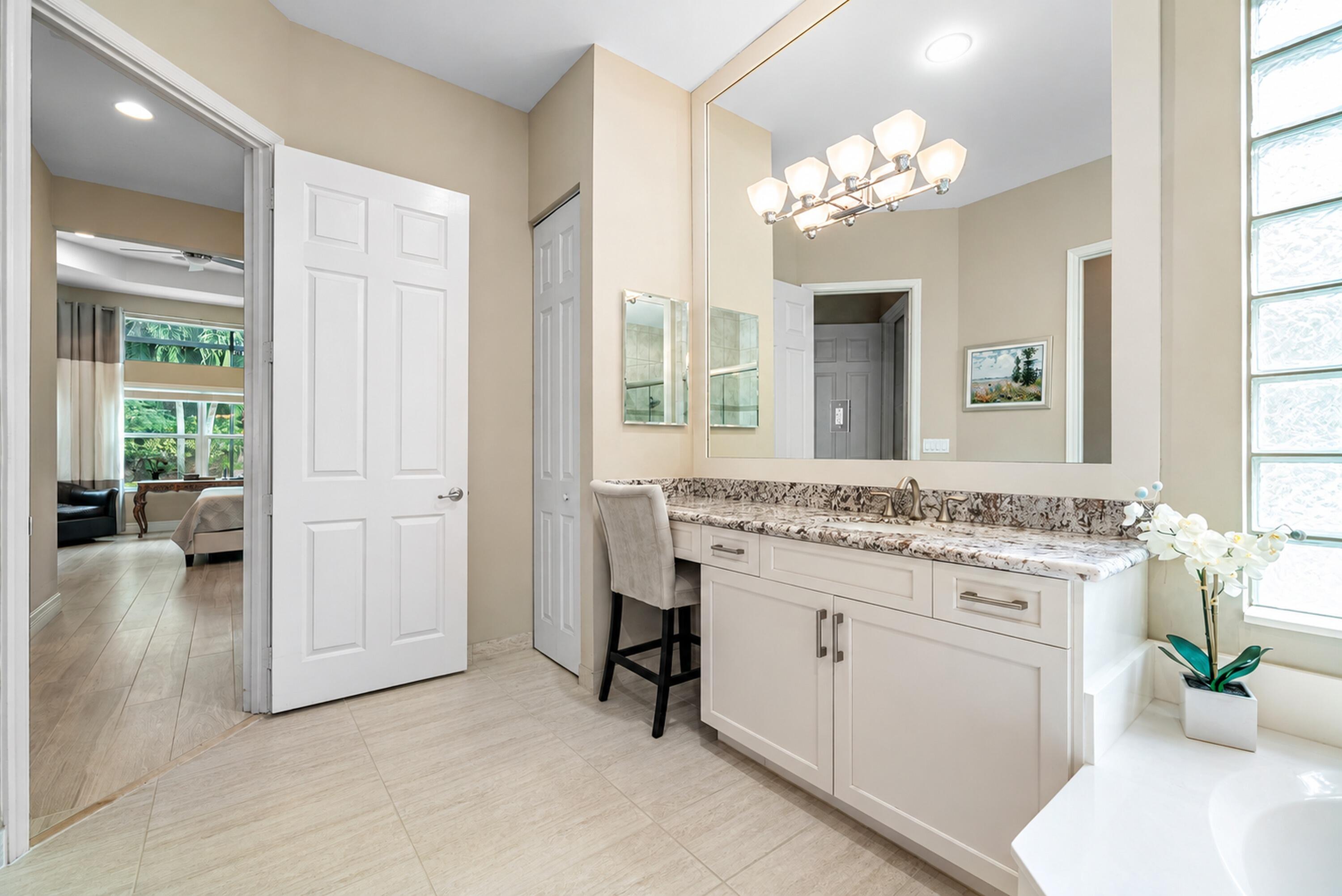 Bathroom vanity featuring white cabinetry, stone-surface countertop with an integrated sink, full-width wall mirror, multi-bulb light fixture, and translucent glass block window