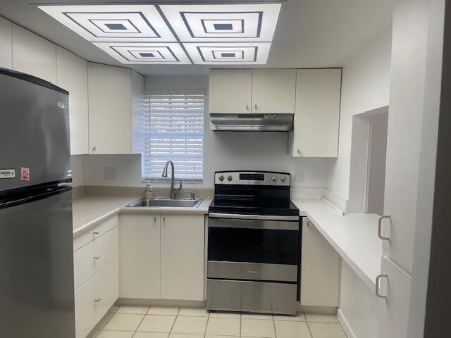 Kitchen featuring white cabinetry, stainless steel appliances, neutral solid-surface countertops, dual-basin sink with arched faucet, and recessed geometric-patterned ceiling lighting