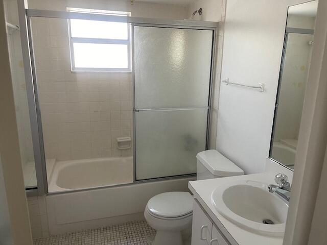 Bathroom featuring a combination bathtub and shower with a sliding glass enclosure, tile wall surround, single-basin vanity with a solid-surface countertop, and a wall-mounted mirror