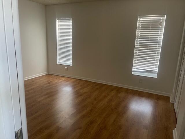 Interior space featuring wood-finish flooring, neutral wall tones, and two windows with horizontal blinds