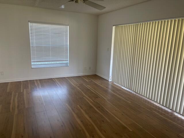 Interior space featuring wood-finish flooring, white walls, a ceiling fan, a standard window with horizontal blinds, and sliding glass doors with vertical blinds