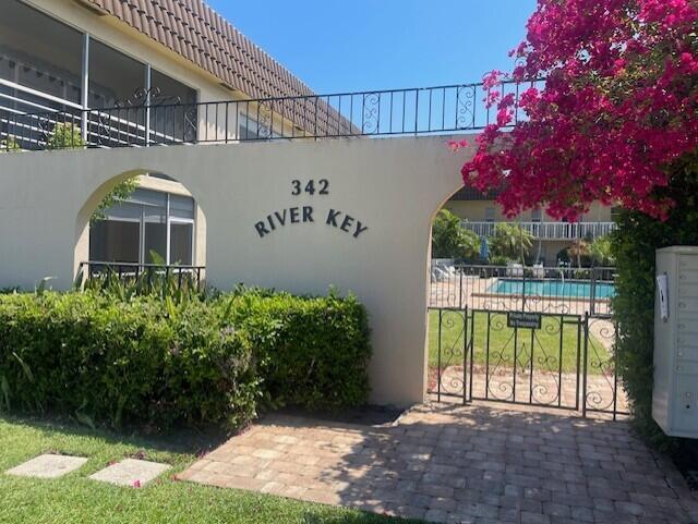 Stucco entrance wall with arched openings, wrought iron fencing, paver pathway, and community swimming pool