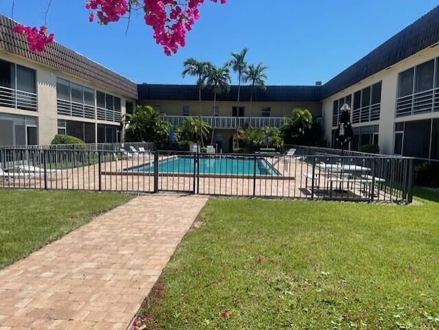 Common swimming pool area featuring a brick paver walkway, manicured lawn, perimeter metal fencing, and mature palm trees