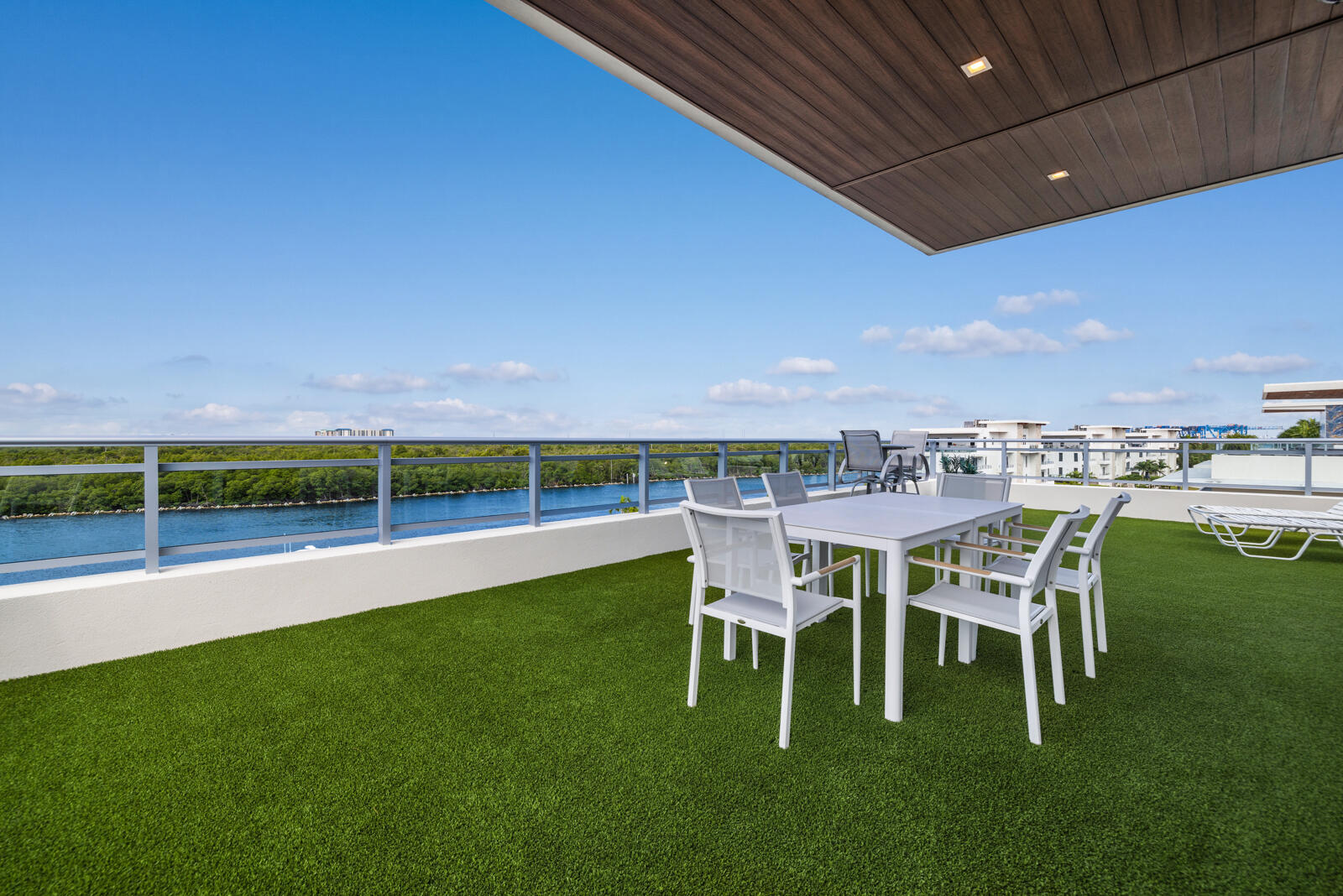 Expansive outdoor terrace featuring synthetic turf, metal railing, recessed lighting, and a wood-finish ceiling panel