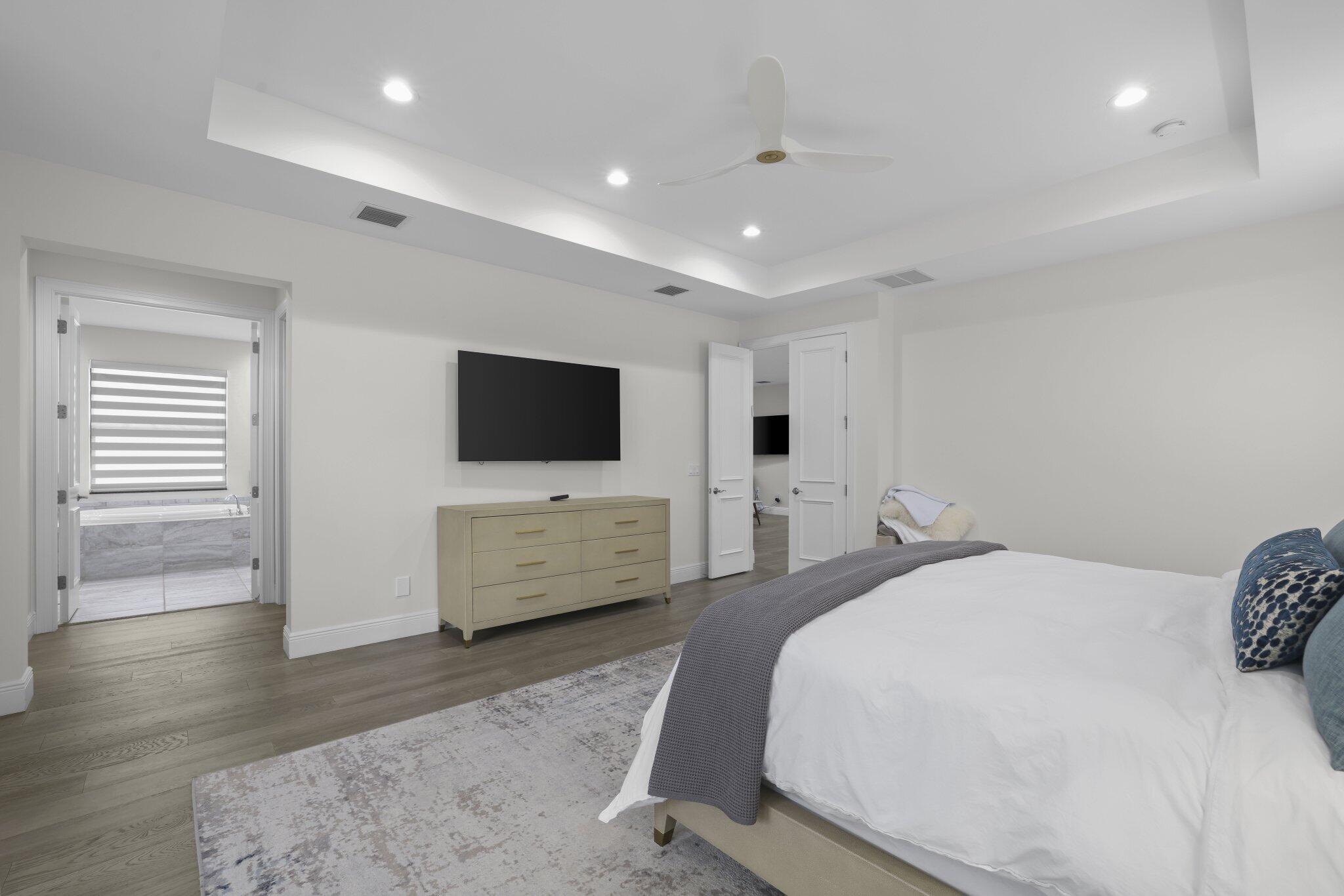 Tray ceiling with recessed lighting and a ceiling fan, wood-finish flooring, and a wall-mounted television