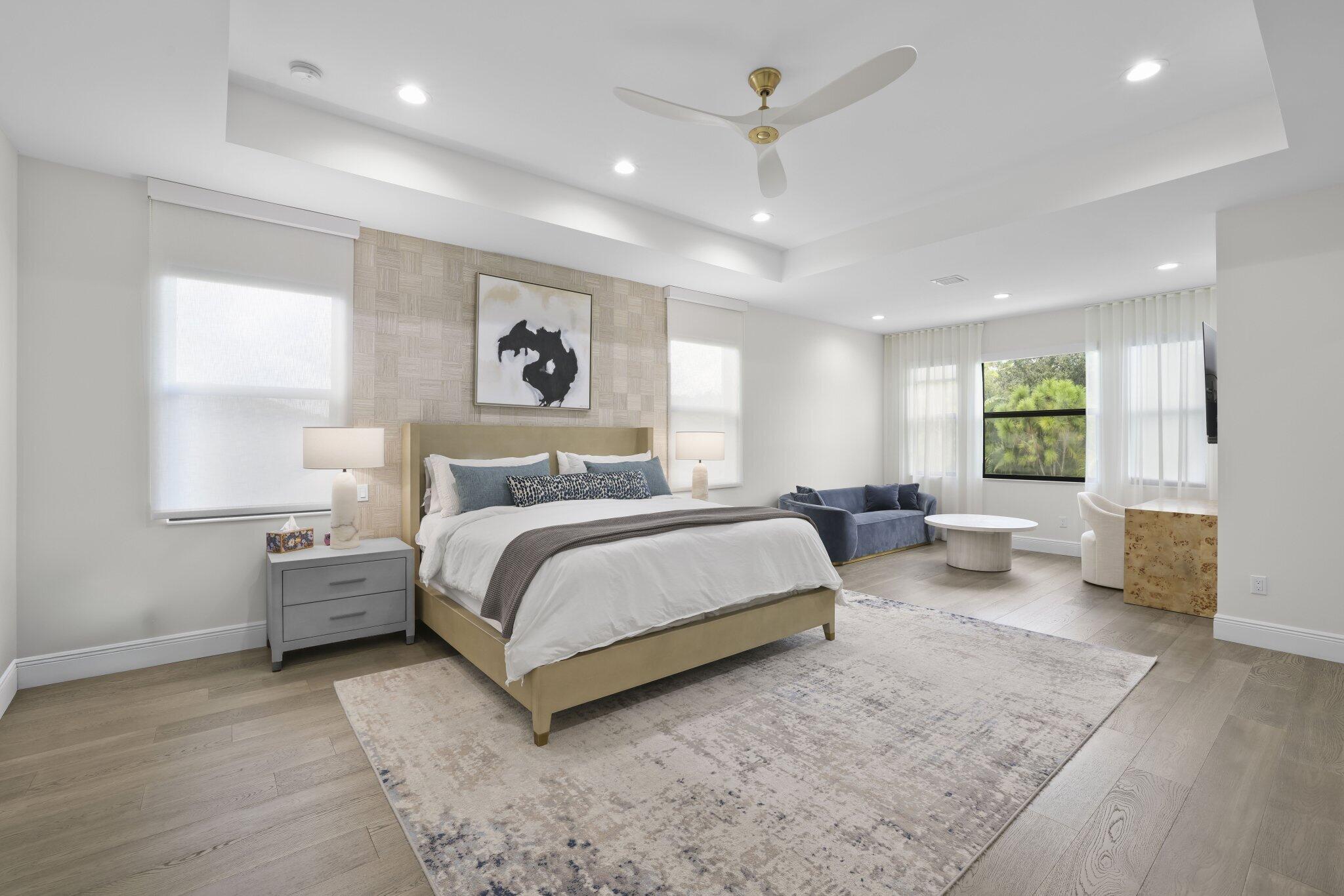 Tray ceiling with recessed lighting, wood-finish flooring, accent wall, ceiling fan, and large windows with roller shades