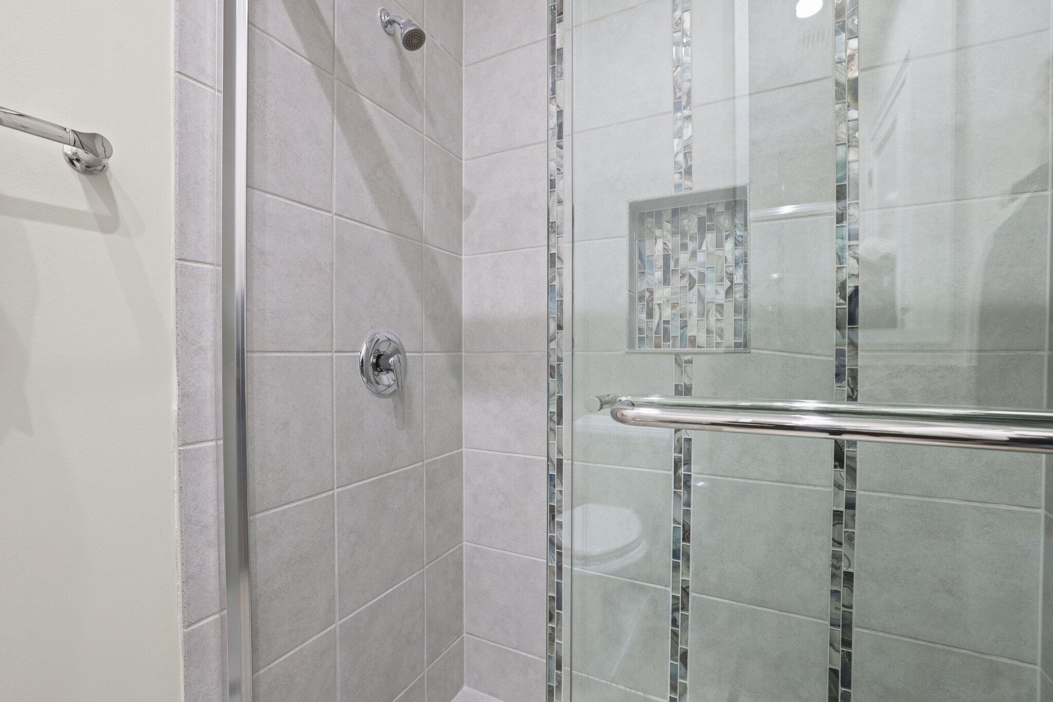 Tiled shower with glass enclosure, chrome fixtures, decorative mosaic tile accents, and a recessed niche