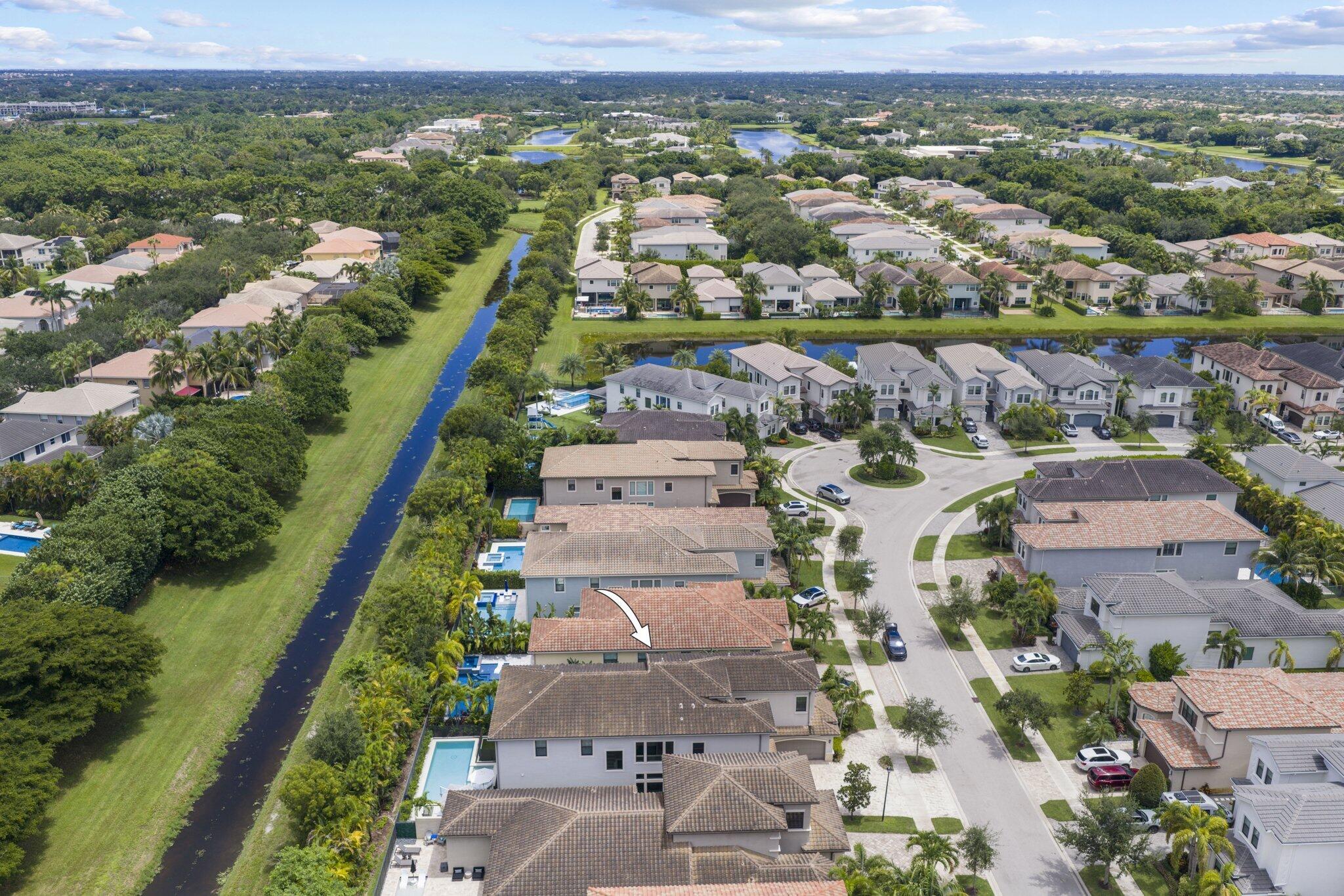 Aerial overview of a residential area with a prominent canal, several homes featuring private pools, and mature landscaping