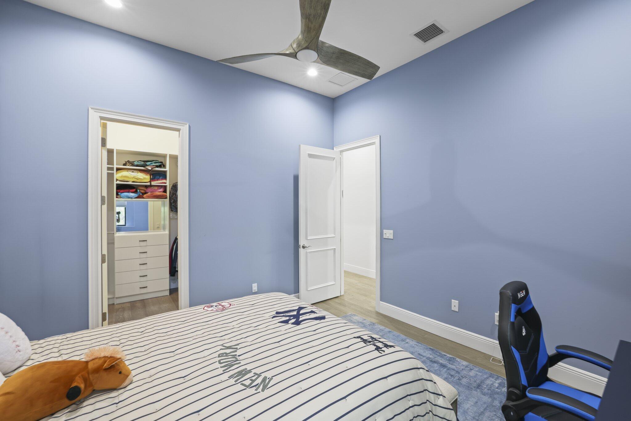 Recessed lighting illuminating the ceiling, a built-in closet system with drawers and shelving, wood-finish flooring, and a modern ceiling fan