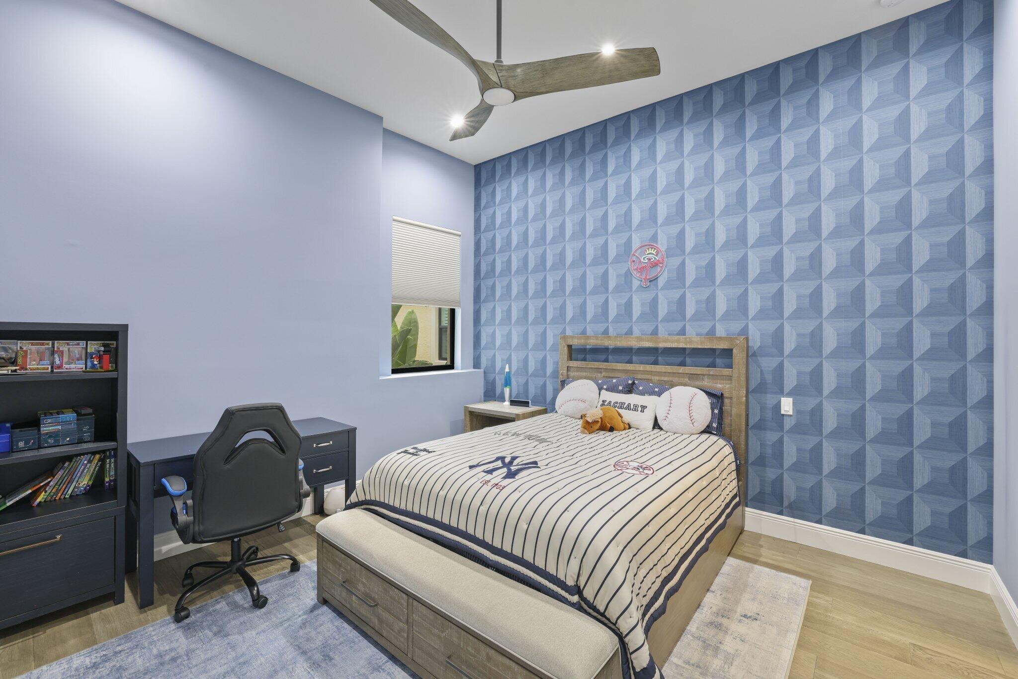 Bedroom featuring a textured accent wall, wood-finish flooring, a contemporary ceiling fan, and built-in desk with shelving