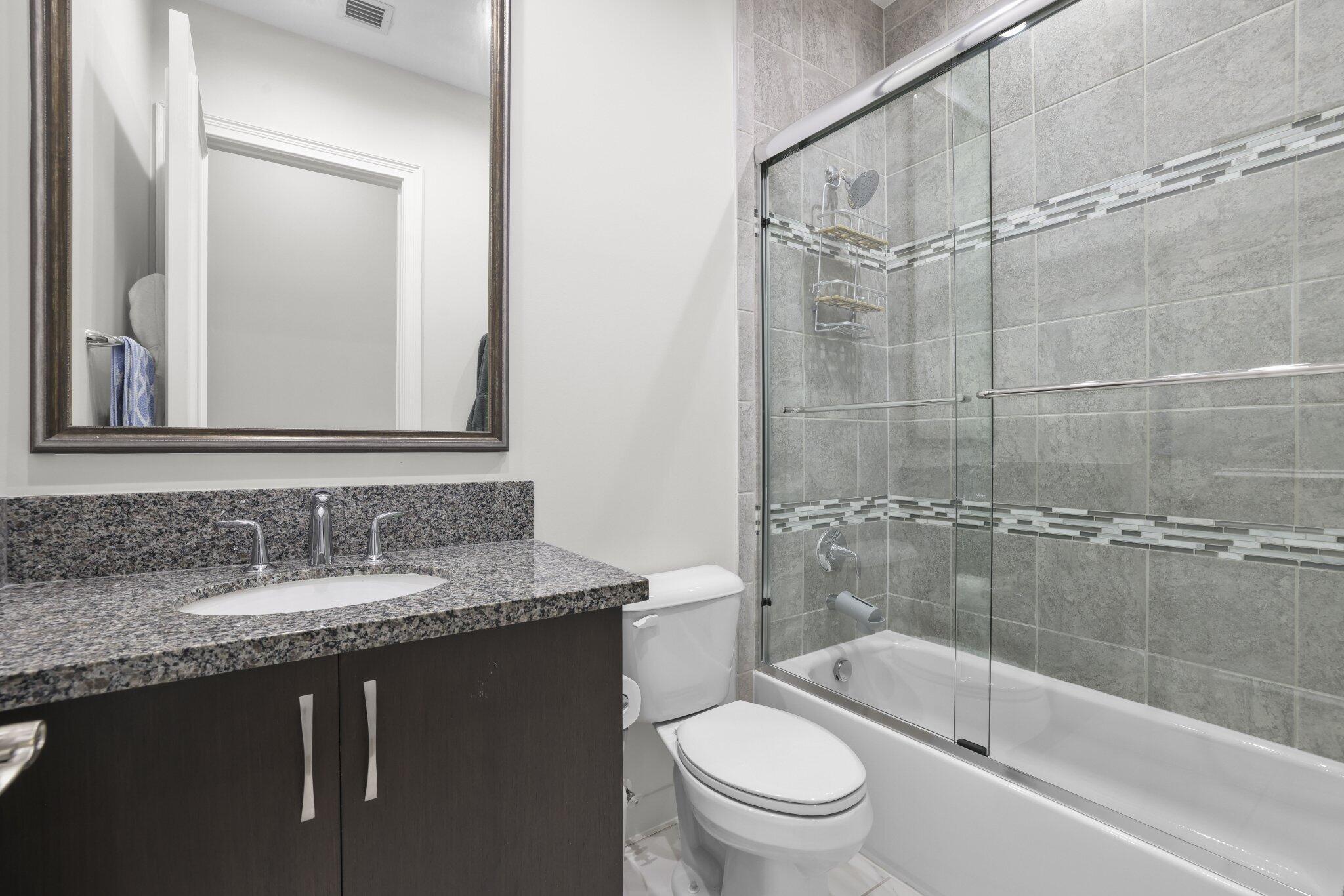 Built-in vanity with a stone countertop and undermount sink, framed mirror, full bathtub, and tiled shower surround with glass sliding doors