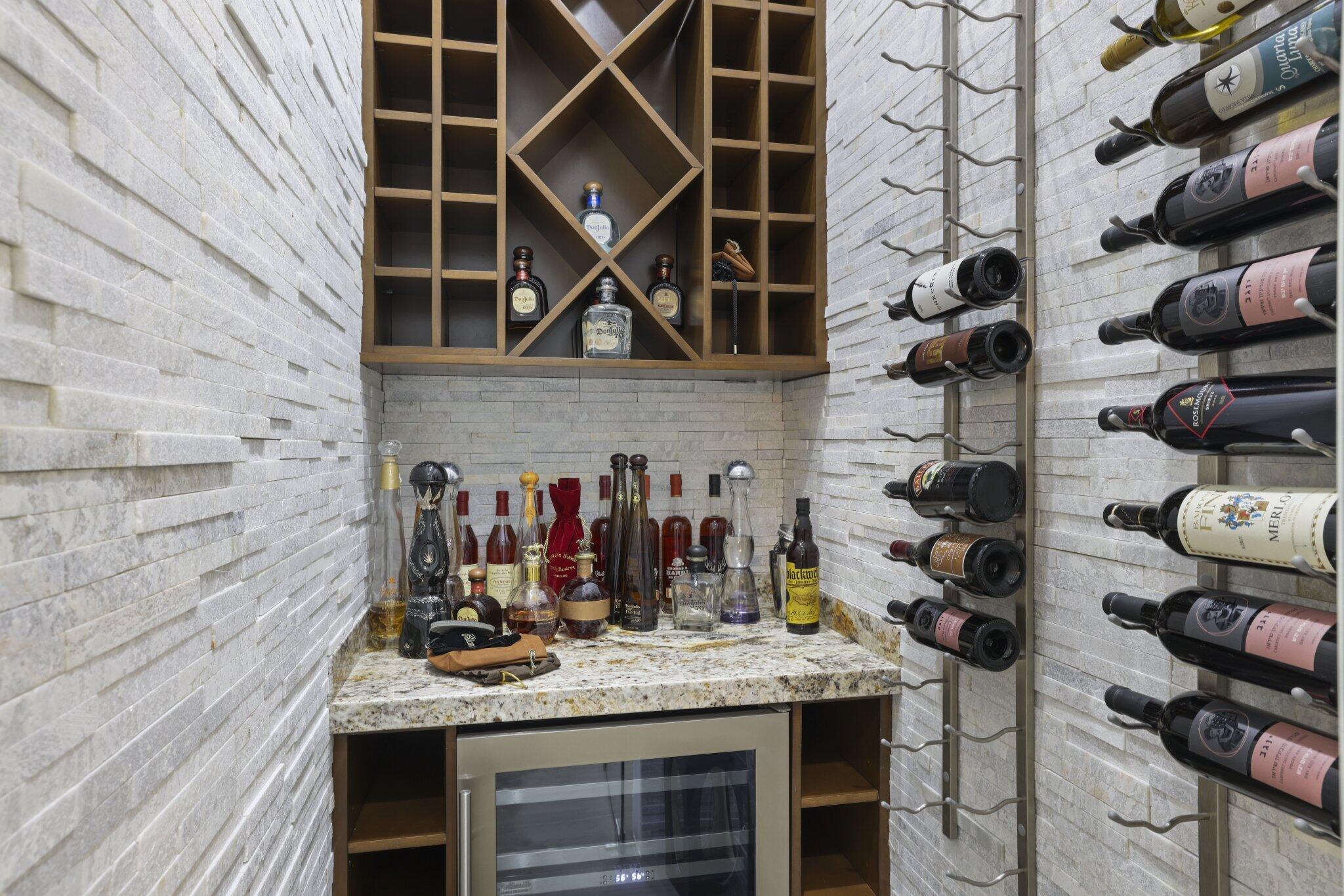 Stacked stone accent walls with built-in wine storage, wood-finish shelving, granite-style countertop, and integrated beverage cooler
