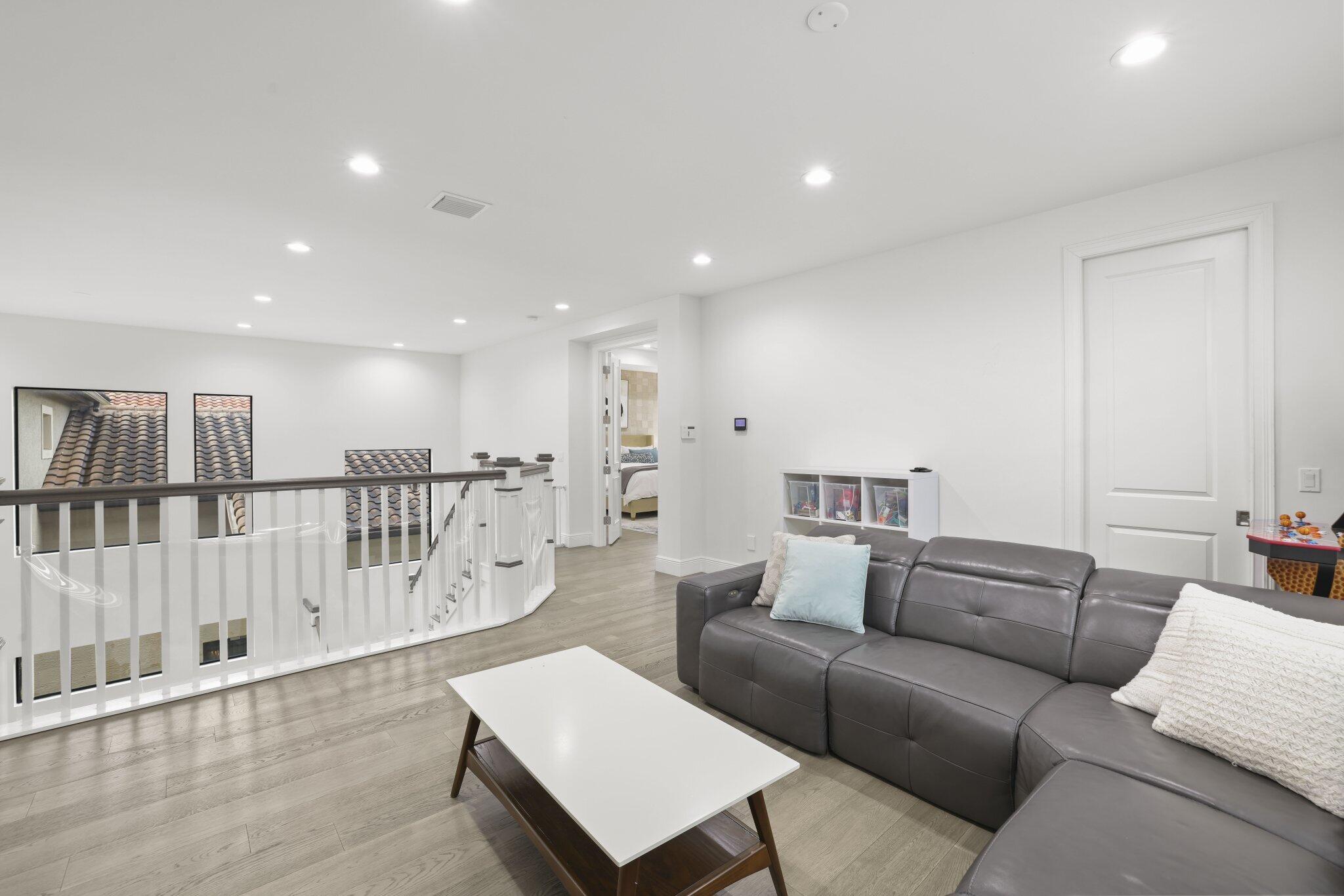 Recessed lighting illuminates the space, featuring wood-finish flooring and a white painted railing