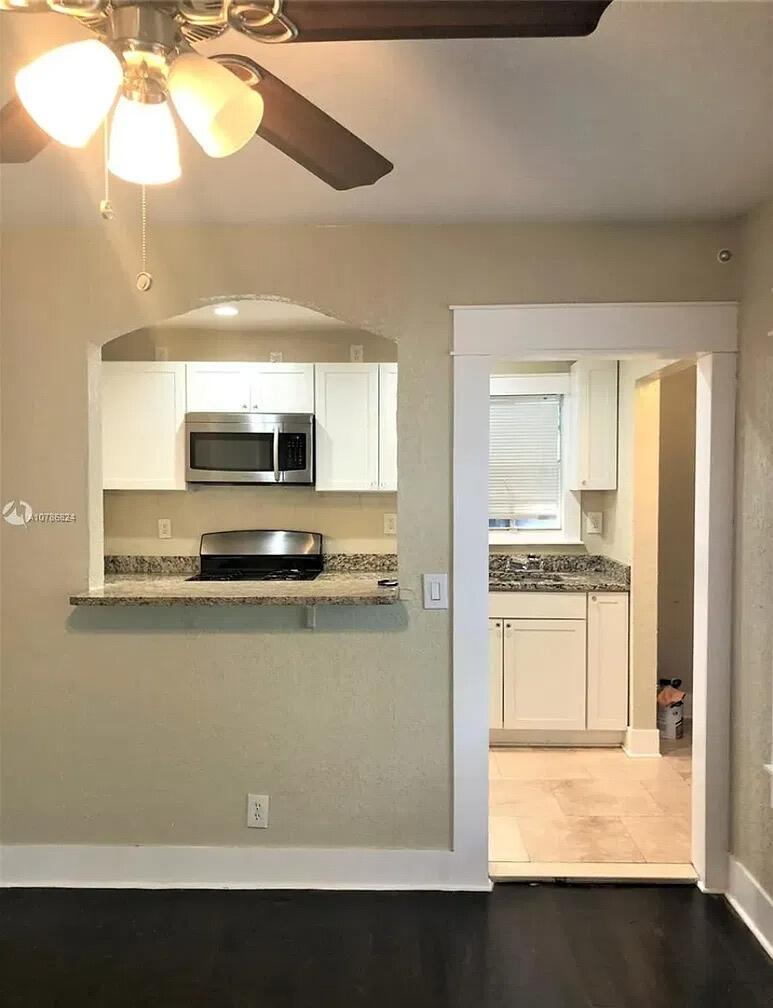 Kitchen featuring white cabinetry, stone-finish countertops, stainless steel microwave, and integrated cooktop with a pass-through opening