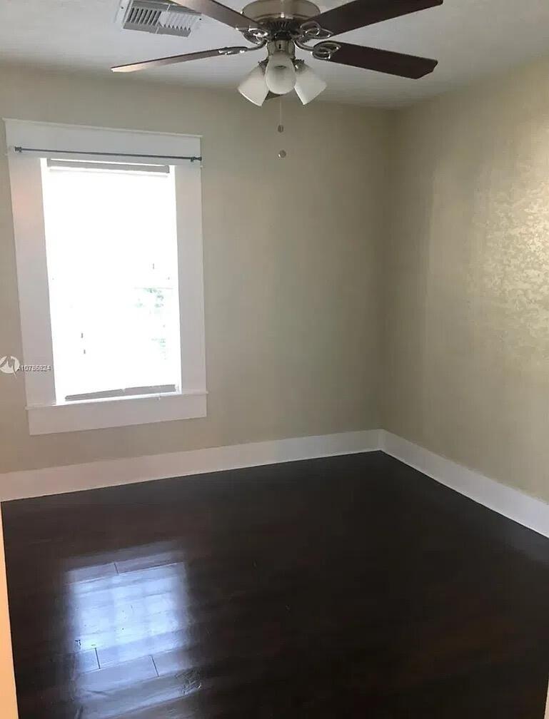 Interior space featuring dark wood-finish flooring, neutral wall tones, white trim, a single-pane window, and a ceiling-mounted fan with integrated lighting