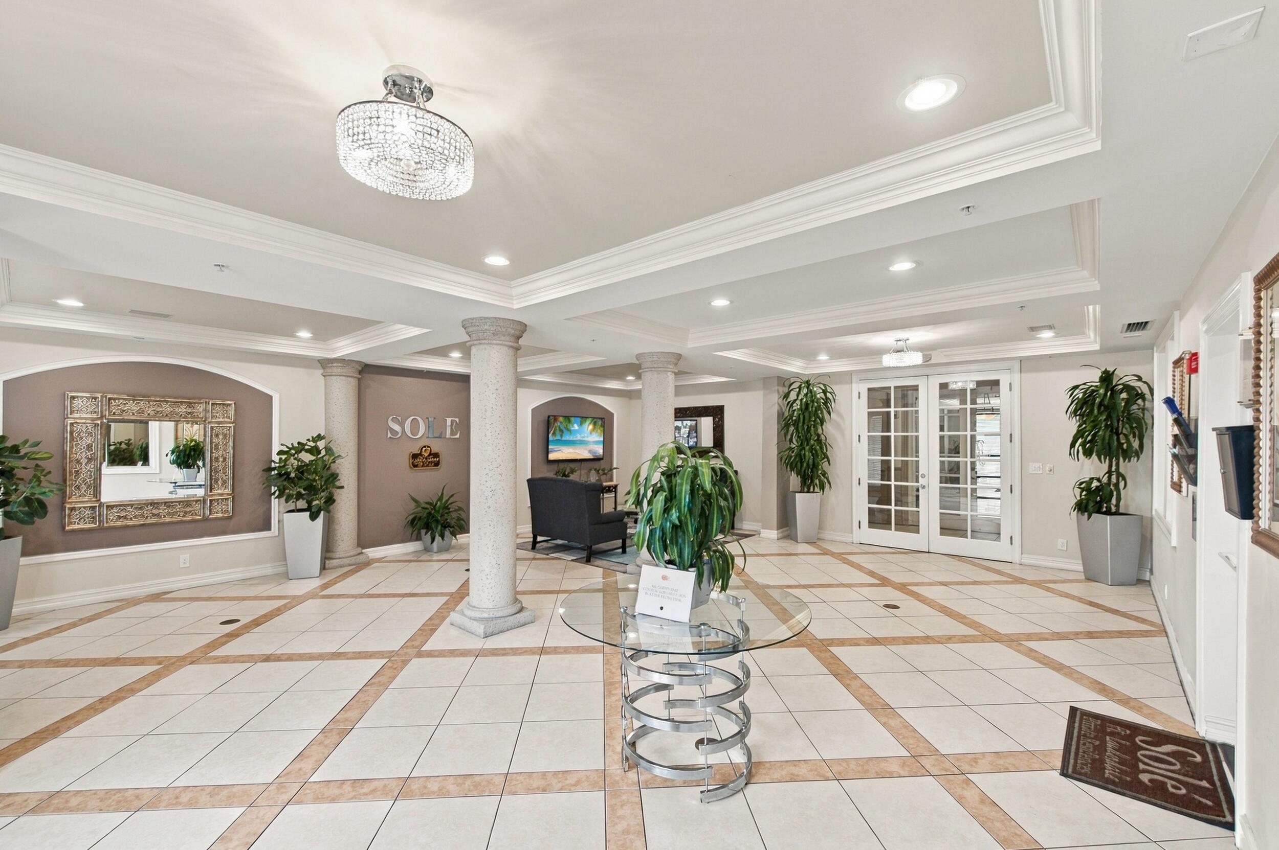 Grand lobby entrance featuring tiered tray ceilings, recessed lighting, ornate crystal-style flush mount fixture, classical columns, and decorative tile flooring with inlaid stone-finish borders