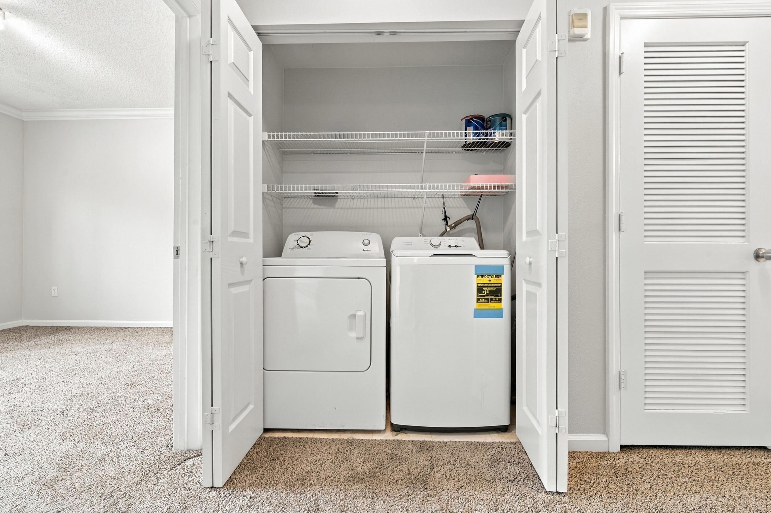 Laundry closet featuring side-by-side appliances, dual wire shelving, and double louvered doors