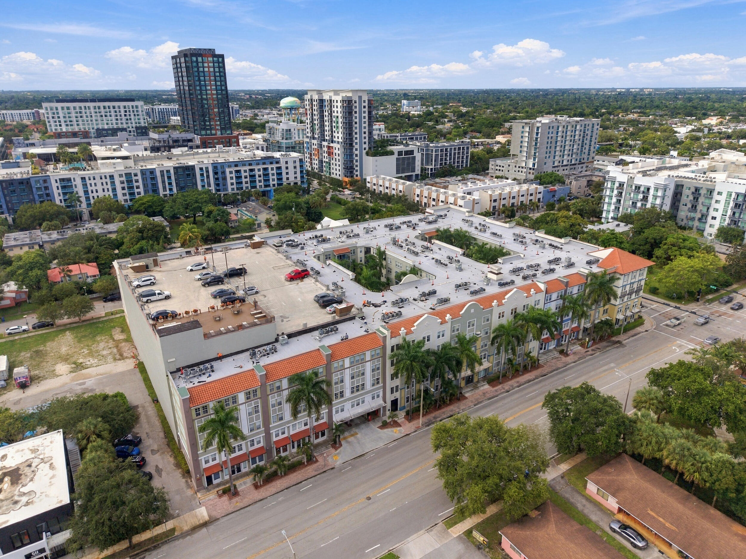 Multi-story building with a terracotta-style tiled roof, stucco-finish facade, structured rooftop parking, and exterior palm tree landscaping
