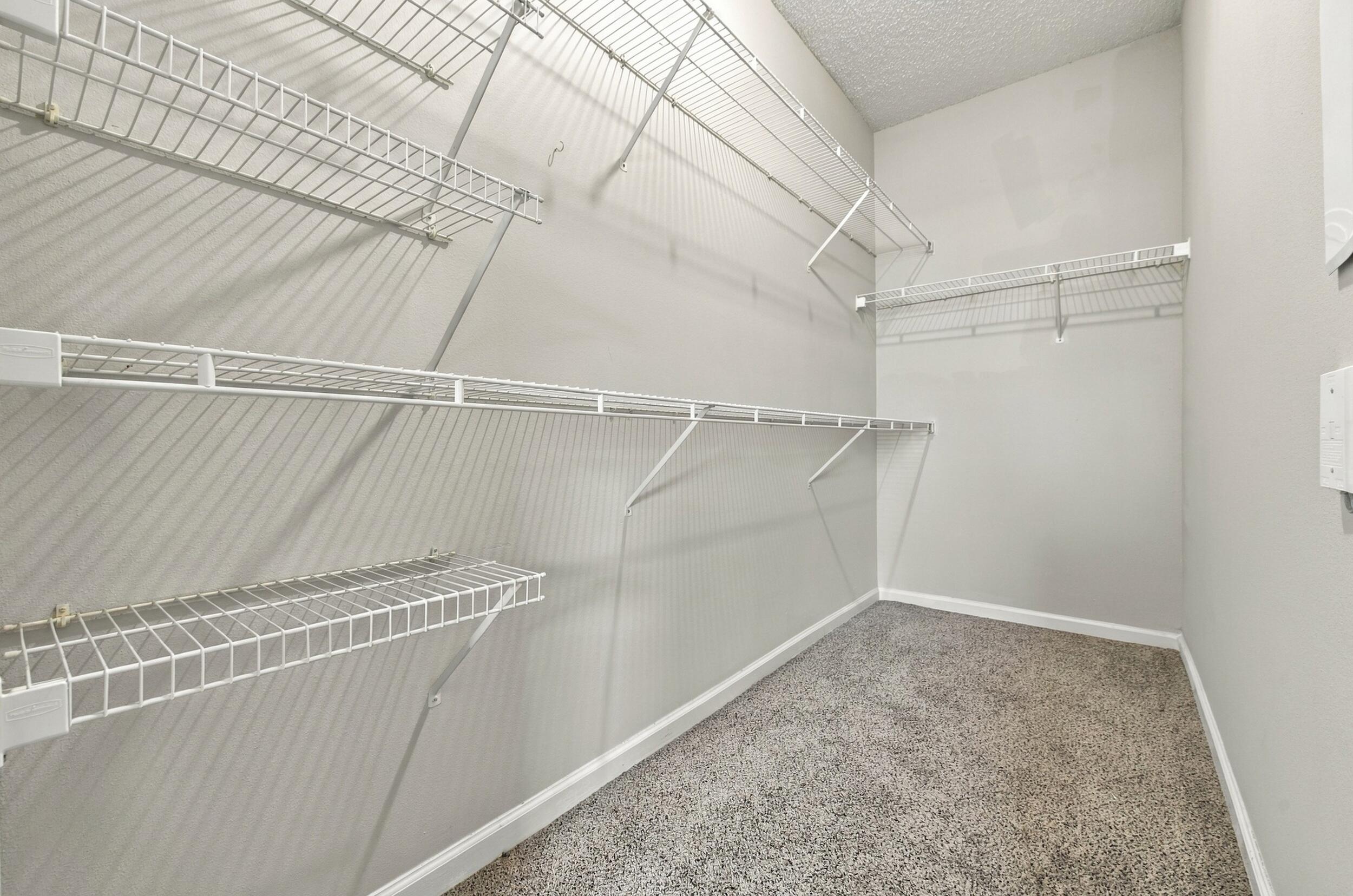 Walk-in storage space featuring neutral wall paint, high-density carpeting, and multi-tier wire shelving systems