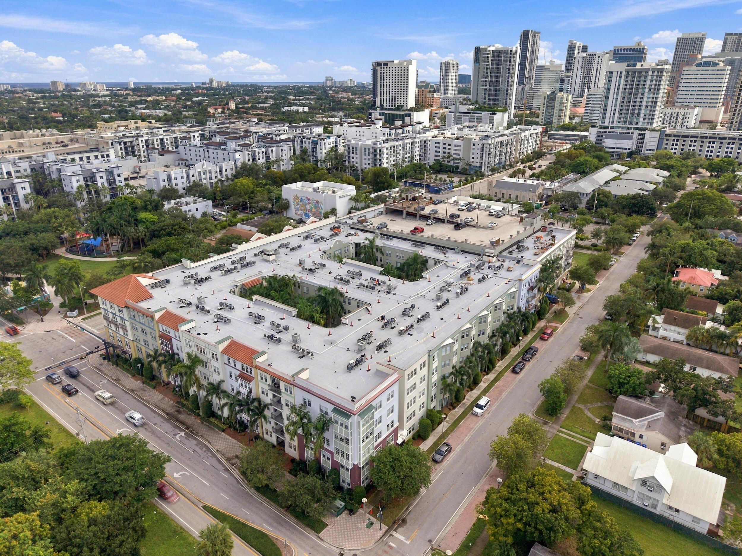 Mid-rise urban residential building featuring a central courtyard, terra cotta roof accents, multi-story masonry construction, and exterior landscaping