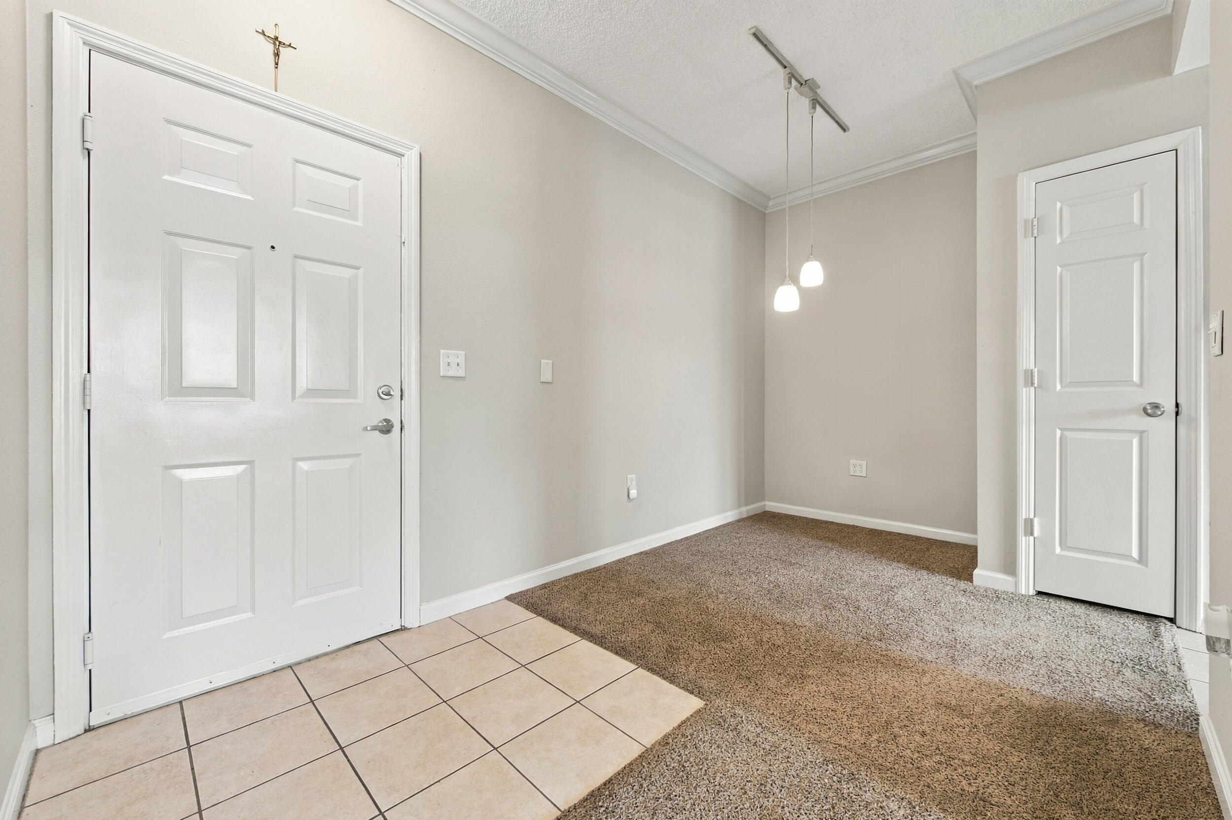 Entryway featuring neutral-toned tile flooring, carpeted floor surfaces, crown molding, a multi-panel door, and a suspended track lighting fixture