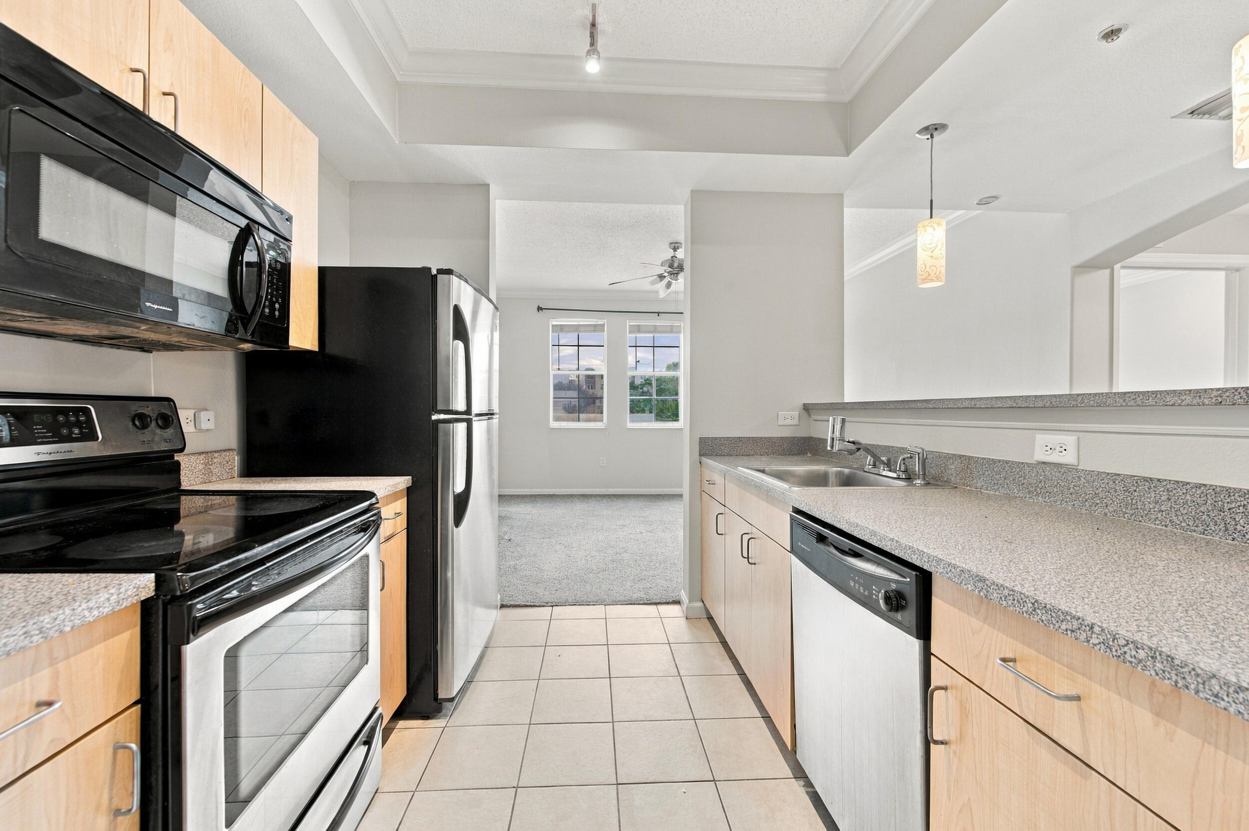 Kitchen featuring light wood-finish cabinetry, solid surface countertops, stainless steel appliances, ceramic tile flooring, and a breakfast bar