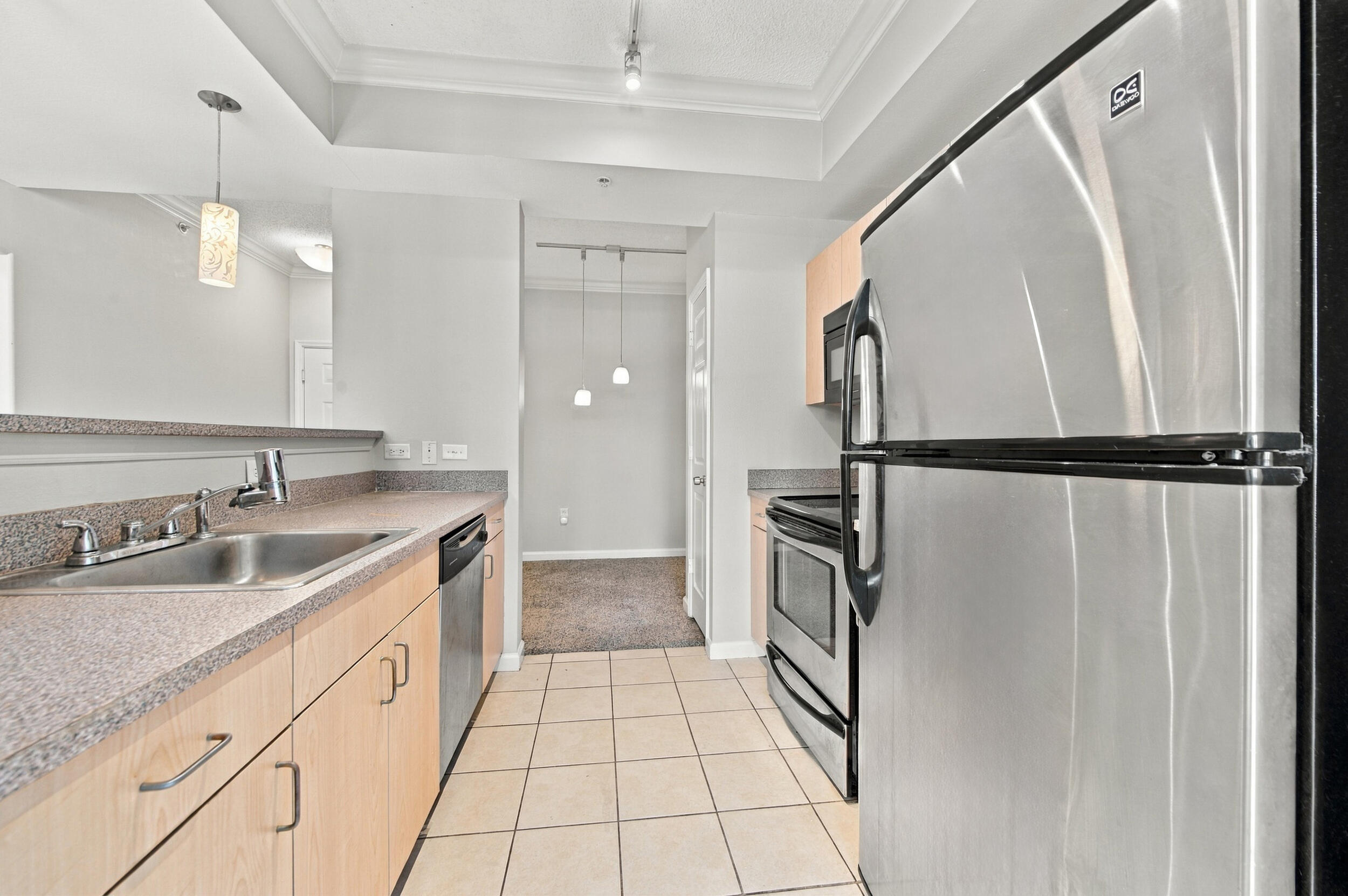 Kitchen featuring stainless steel appliances, light wood-finish cabinetry, solid surface countertops, ceramic tile flooring, and a recessed ceiling design
