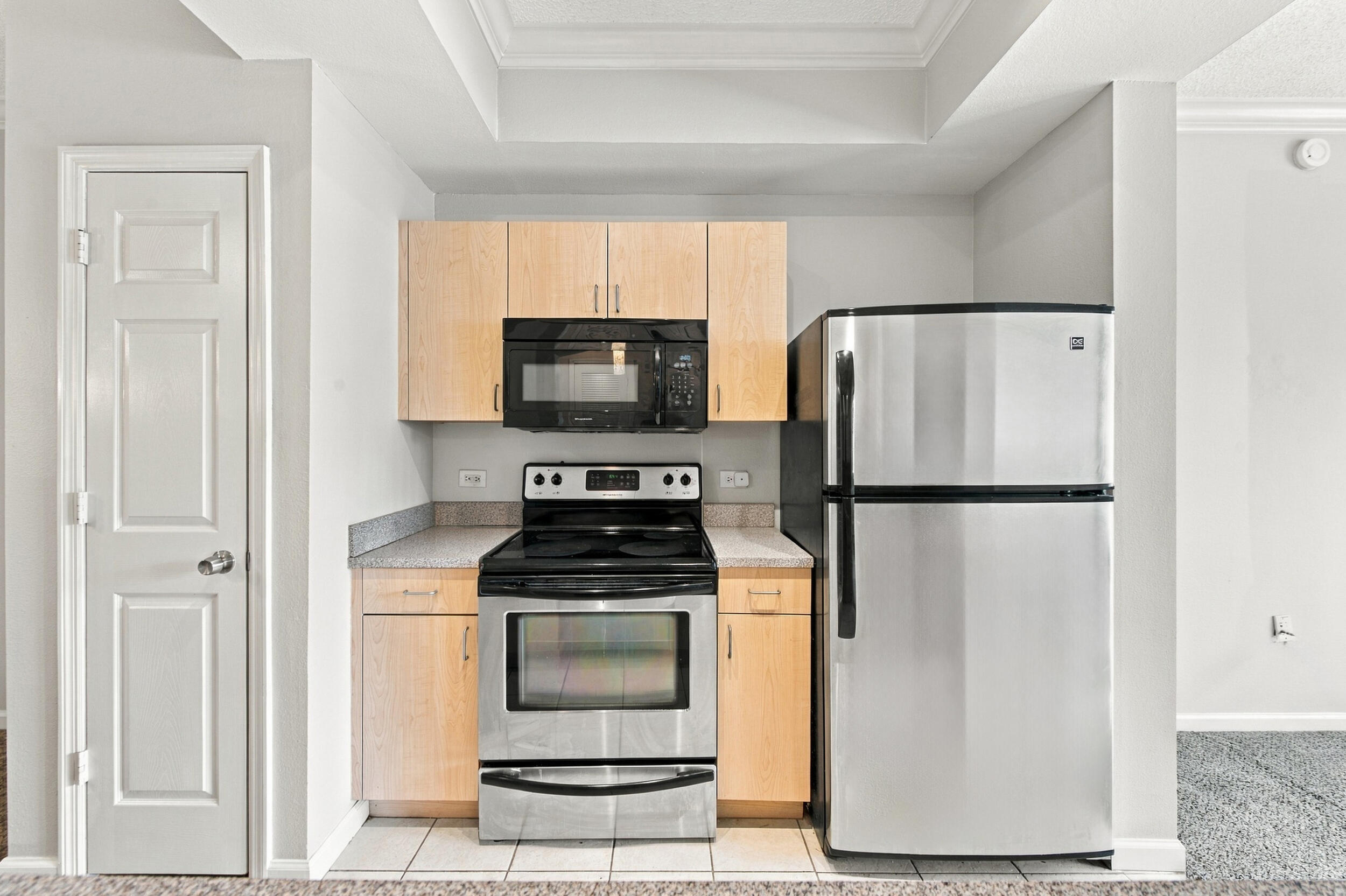 Kitchen featuring light wood-finish cabinetry, stone-texture countertops, built-in microwave, stainless steel range, and stainless steel refrigerator