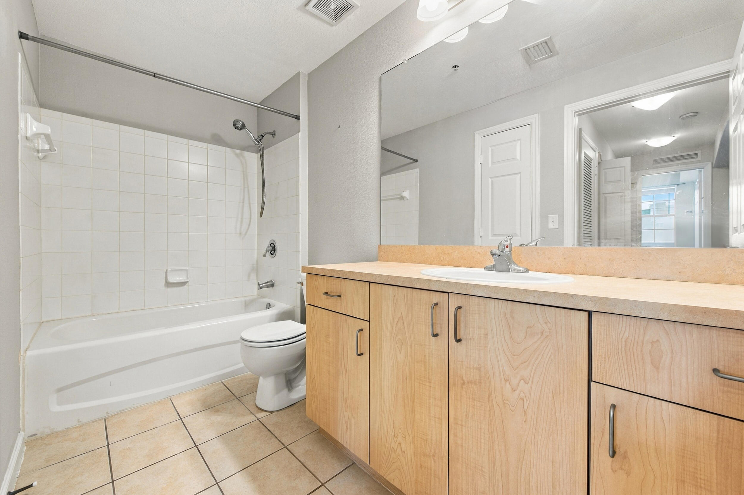 Bathroom featuring a light wood-finish vanity, solid-surface countertop with an integrated basin, oversized wall-mounted mirror, and tile flooring