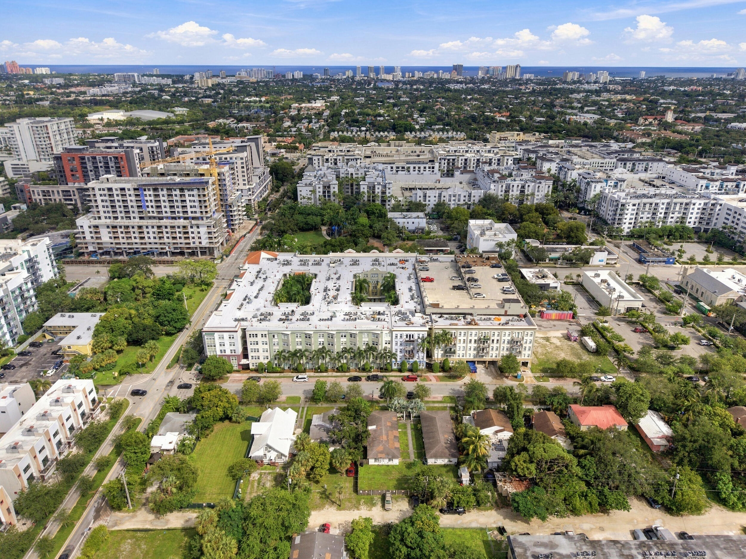 Aerial perspective of mid-rise multi-story residential building featuring dual internal courtyards, ground-level parking, and mature palm landscaping
