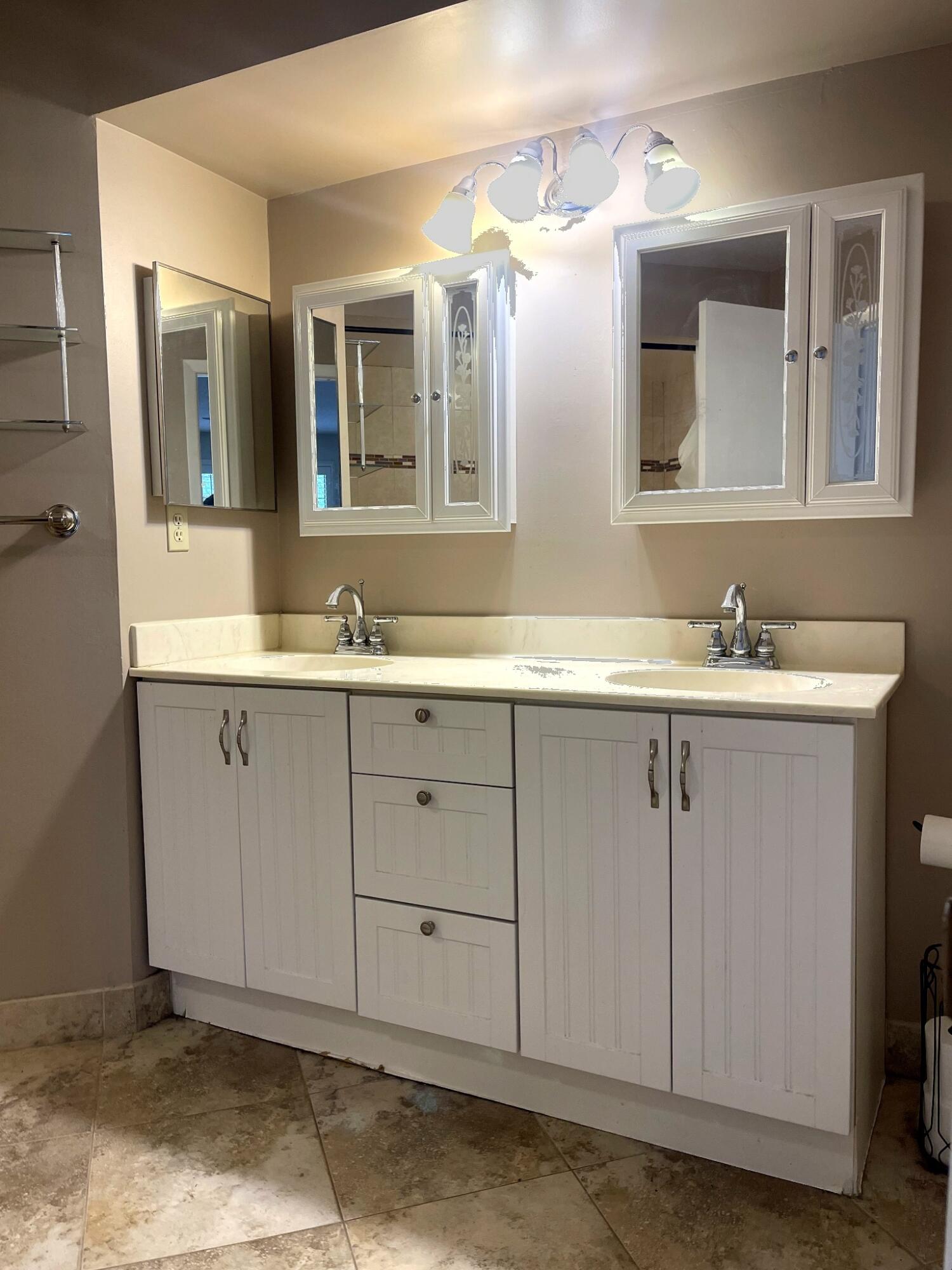 Double vanity featuring white cabinetry, stone-finish countertops with dual integrated sinks, polished chrome hardware, and wall-mounted medicine cabinets