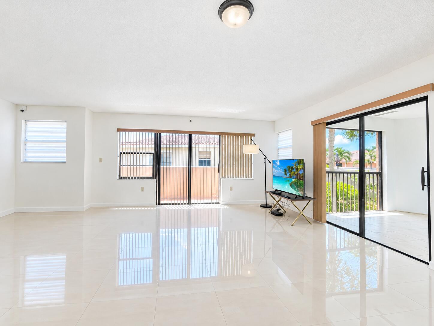 Polished light-toned tile flooring, floor-to-ceiling sliding glass doors, horizontal window blinds, and a flush-mount ceiling light fixture